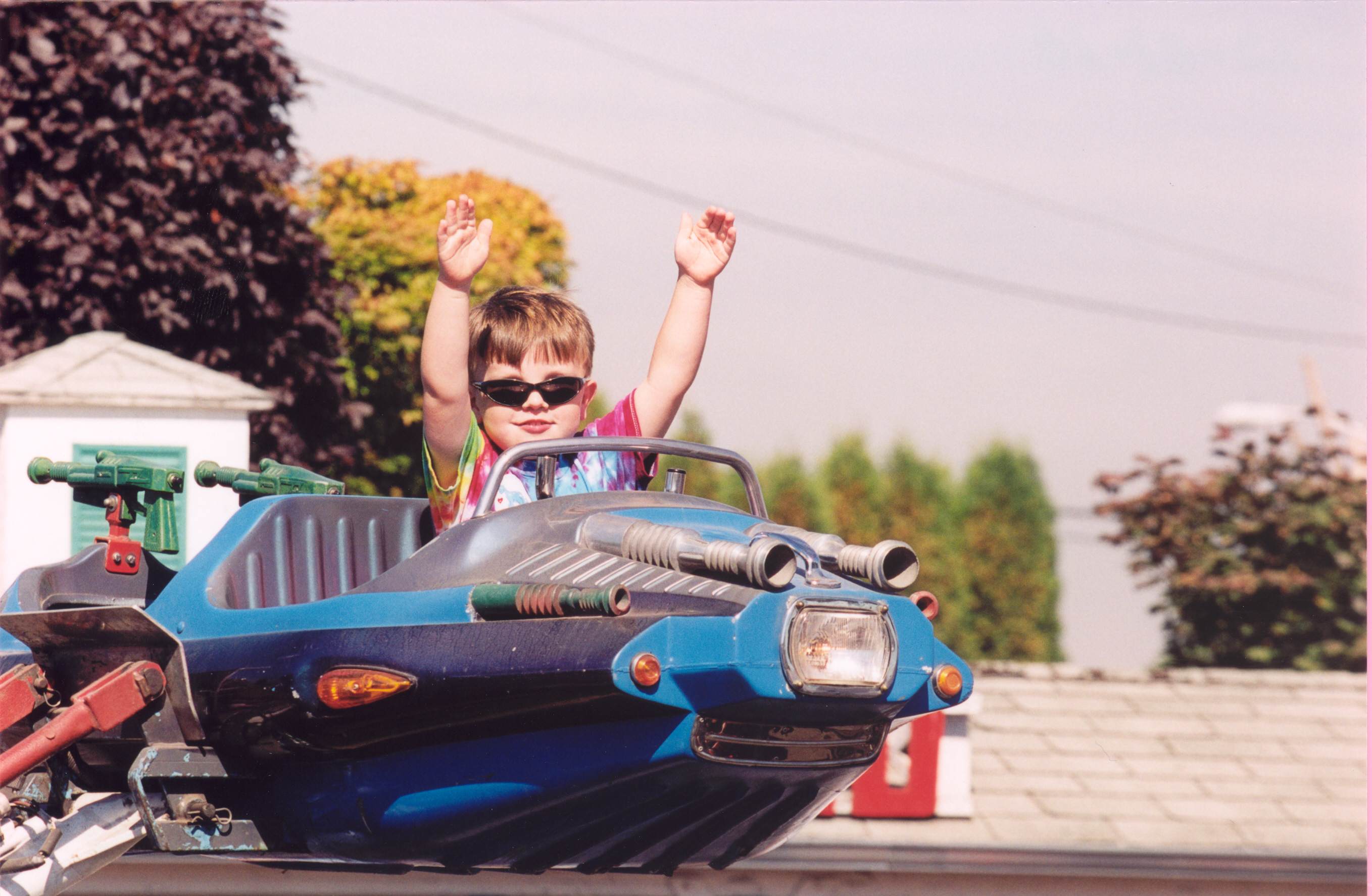 A kiddo in sunglasses rides the Sky Fighter, a ride with a spaceship cart.