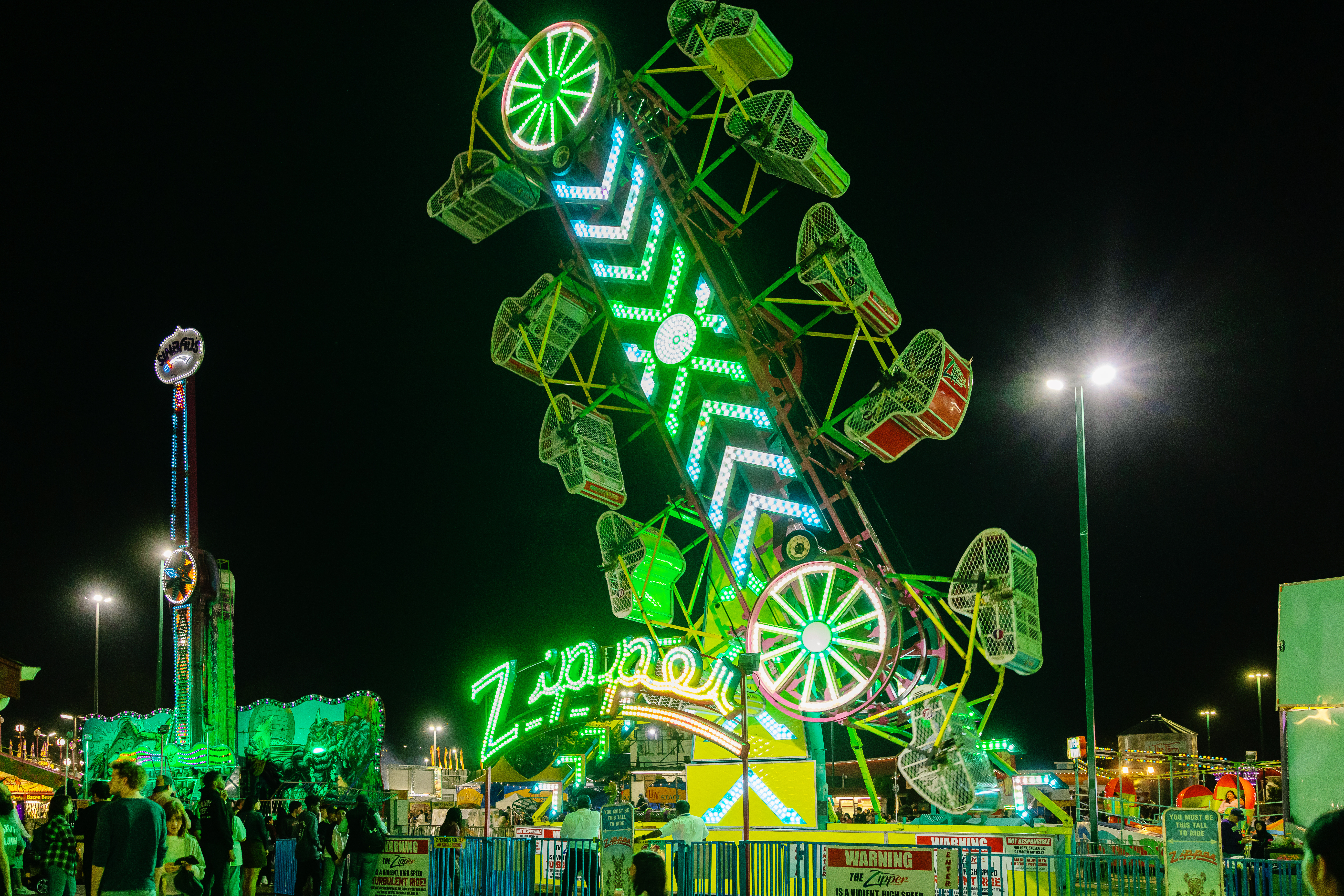 The Zipper, a green glowing ride, places riders in free-spinning cages as it rotates in a vertical circle