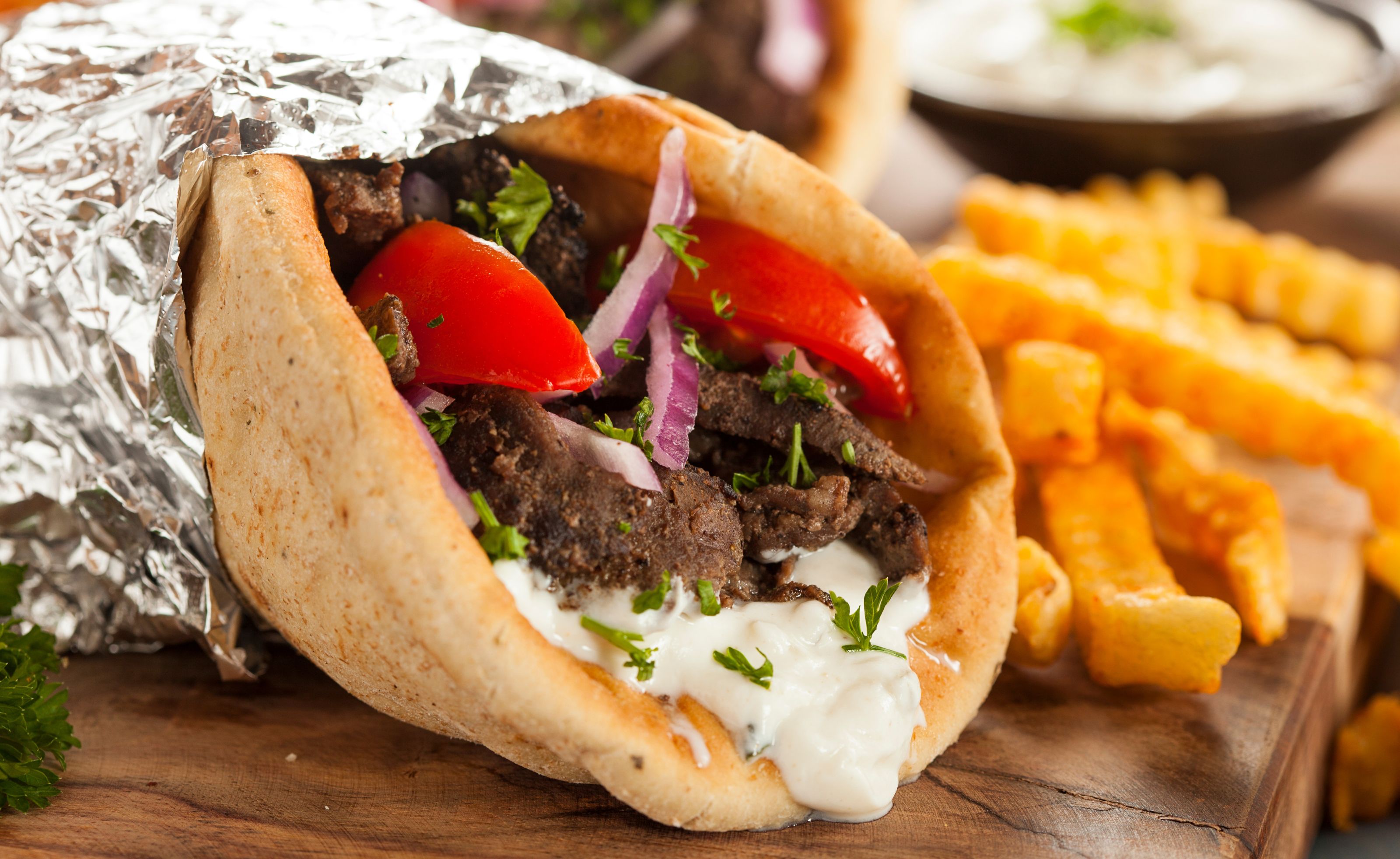 A photo of a gyro in foil with crinkle fries next to it