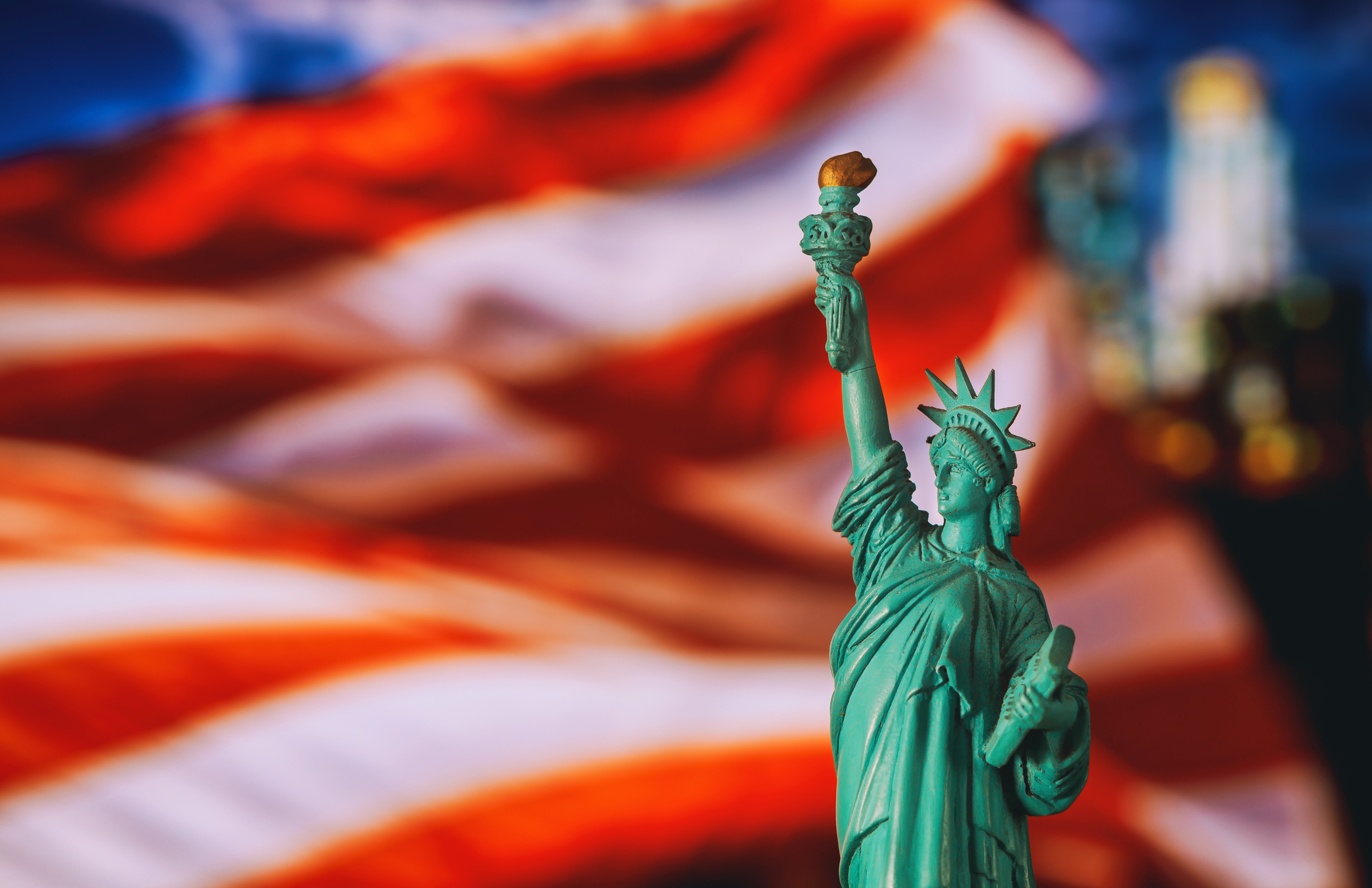 A mini figure of the Statue of Liberty in front of an American flag background.