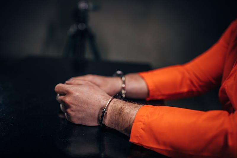 A man in orange jumpsuit and handcuffs