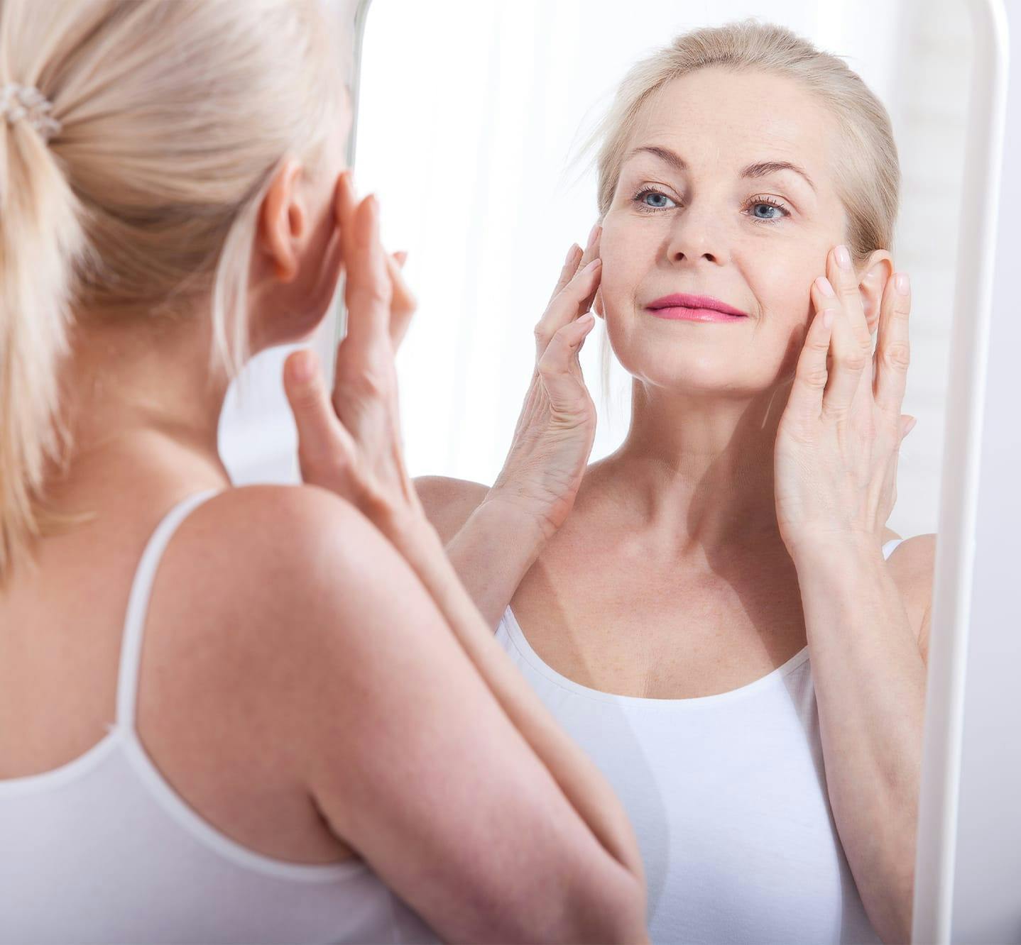 woman touching sides of face in mirror