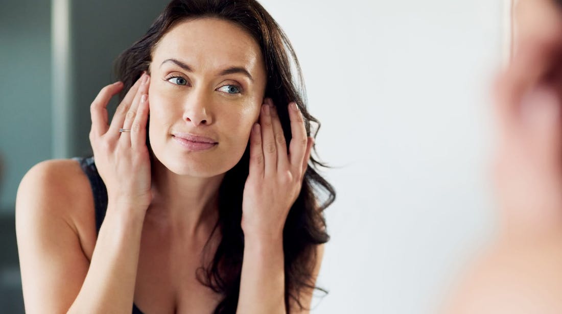 woman inspecting face in mirror