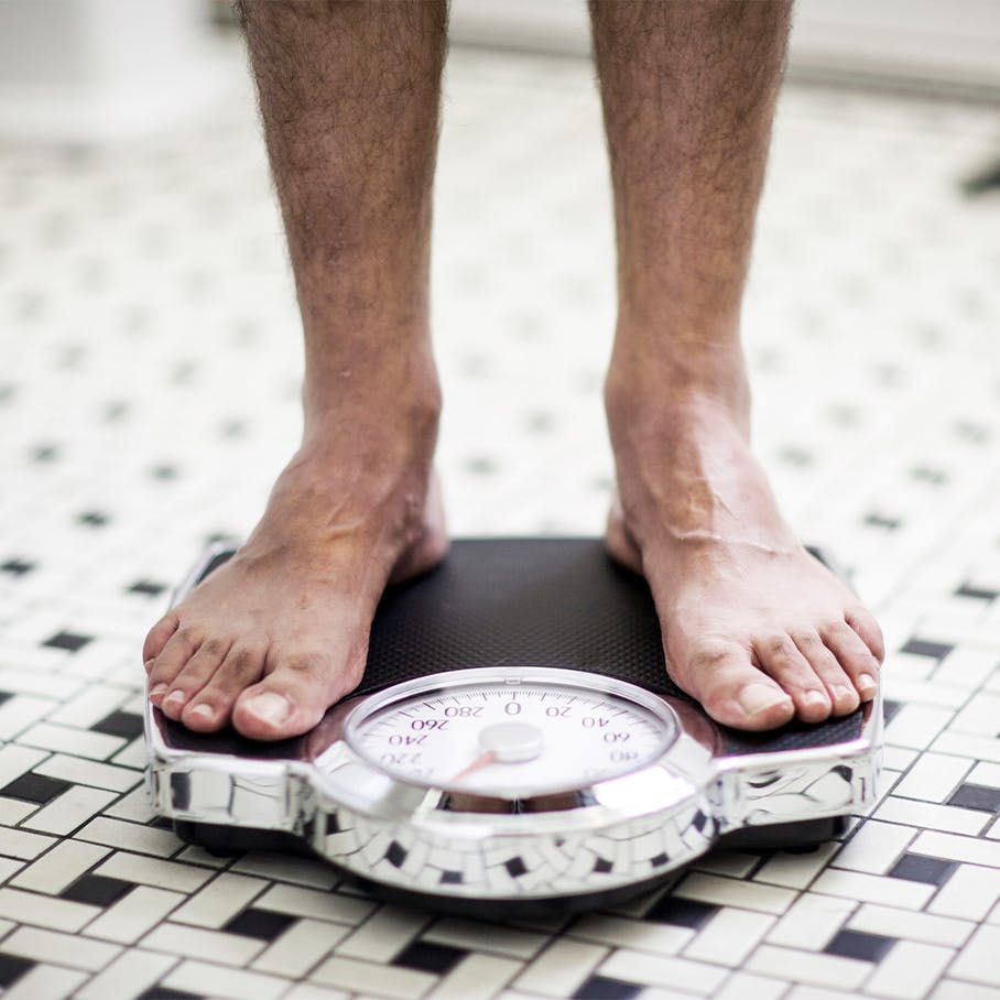 man weighting himself on scale after weight loss in Windermere, FL