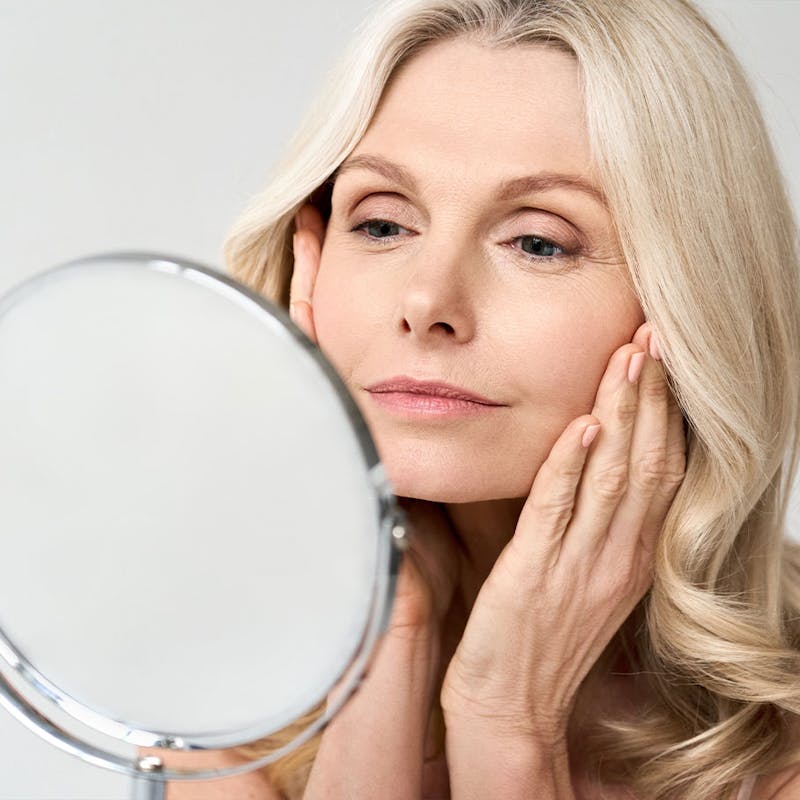 Happy woman looking in the mirror after receiving dermal fillers from Serotonin Centers.