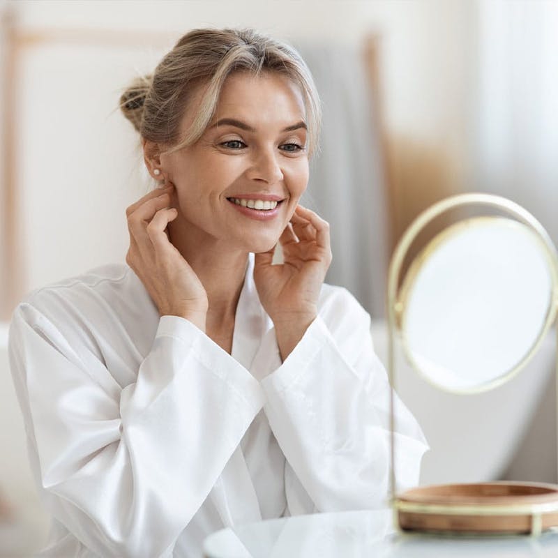 Woman smiling and looking in mirror after Botox treatment at Serotonin Centers.