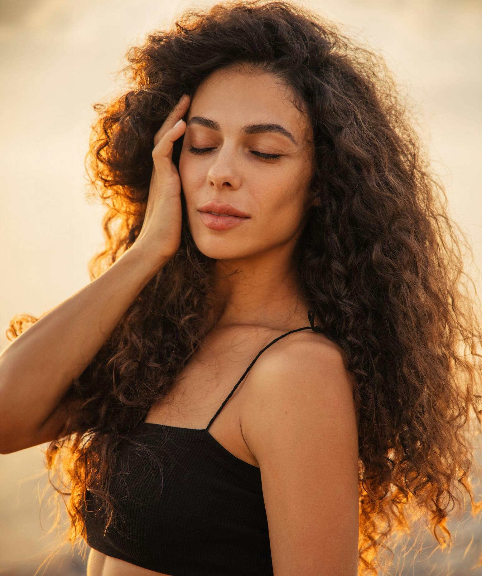 woman with long curly hair, touching her face with her hand