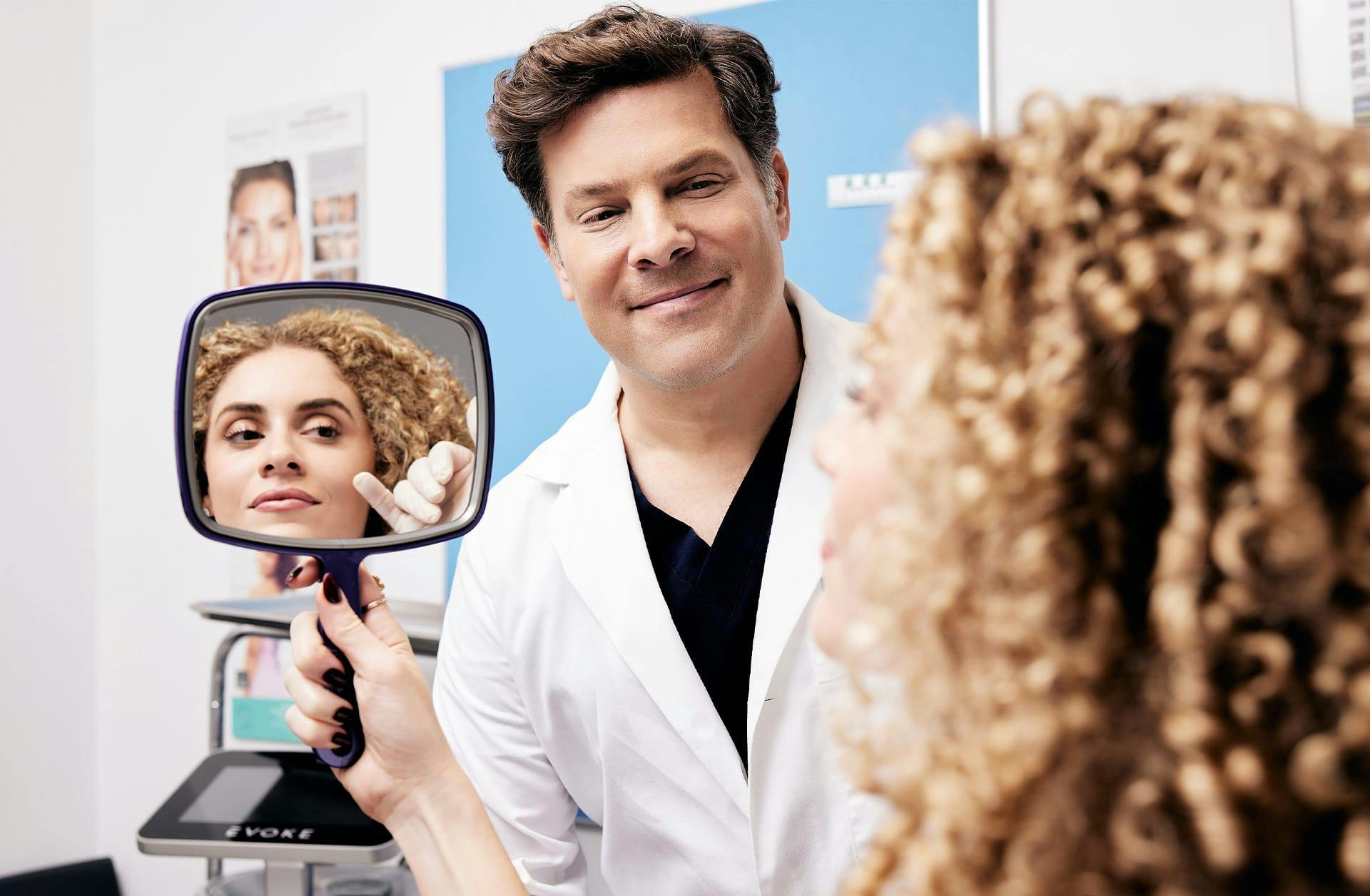 doctor showing patient her facial results on a handheld mirror