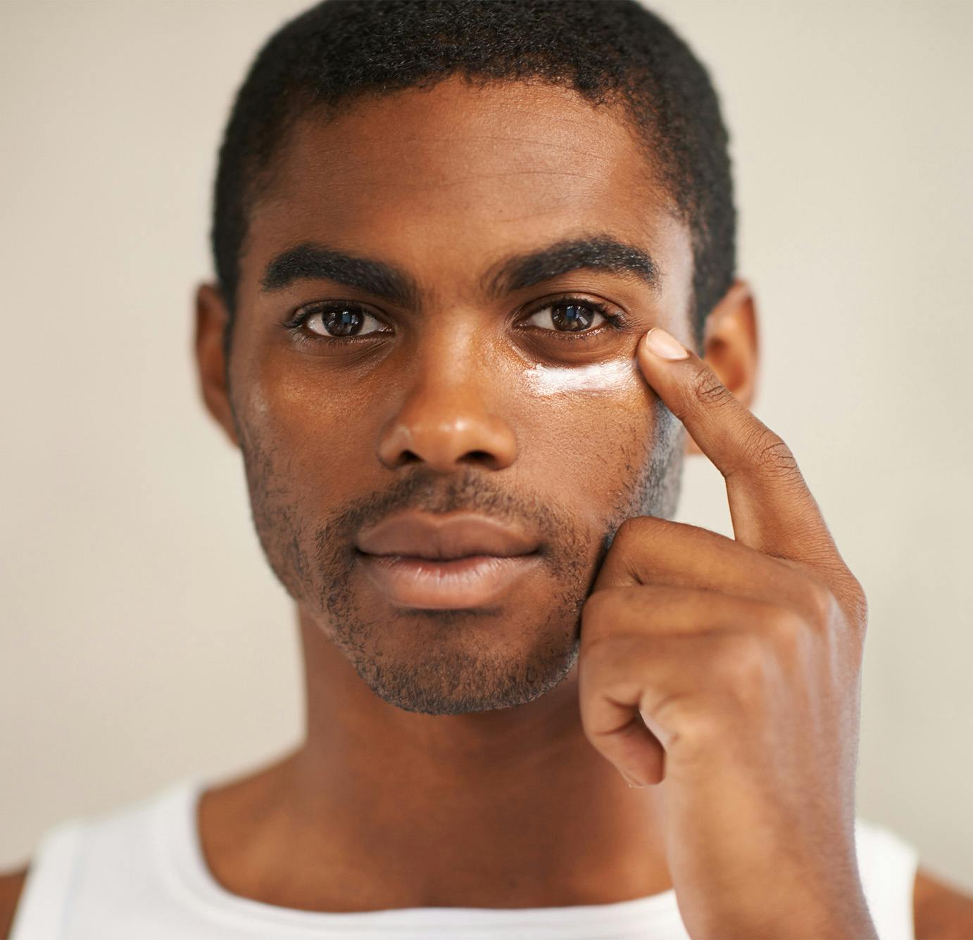 man putting cream on his under eye