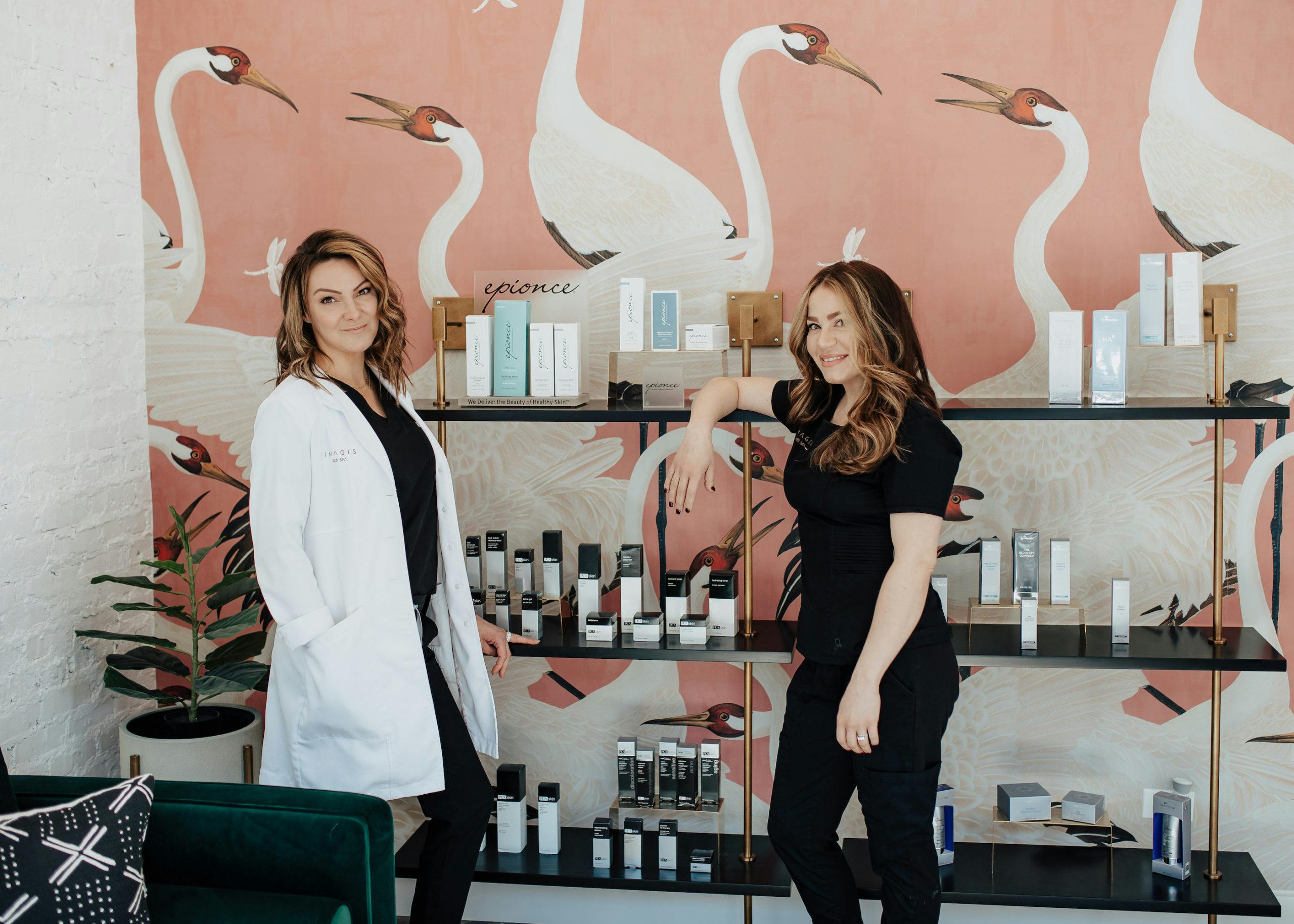 two women posing in front of a shelf with skincare products