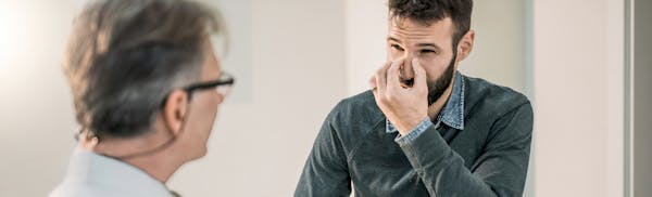 man touching the bridge of his nose in discomfort