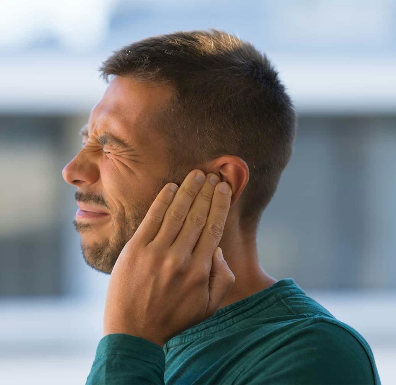 man touching his ear in discomfort