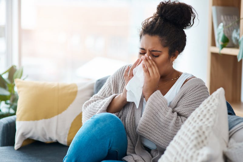 woman blowing nose on couch