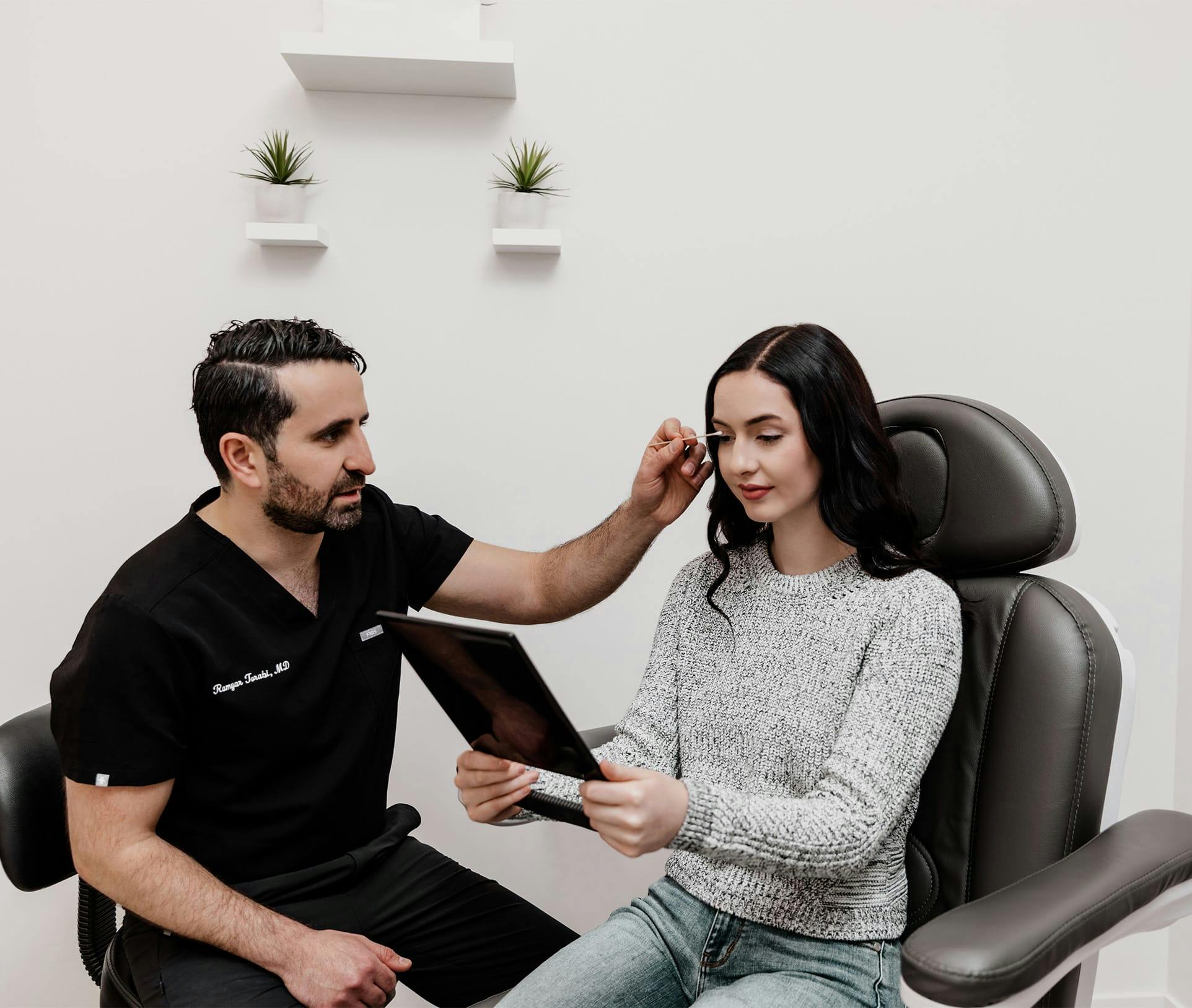 doctor pointing at patient's eyes while patient is looking in hand mirror
