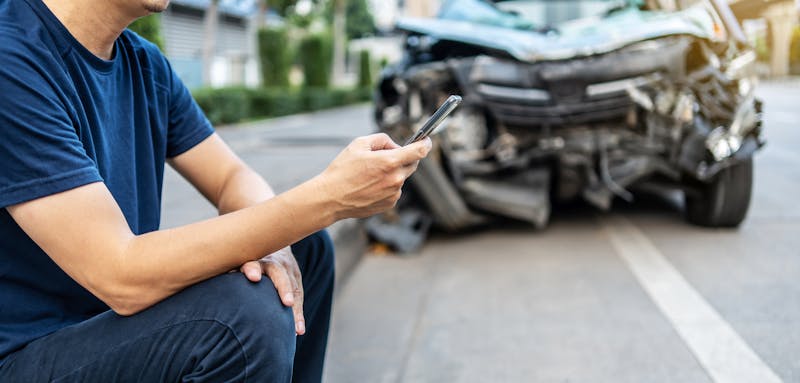 Man calling with phone to his insurance agent after traffic accident