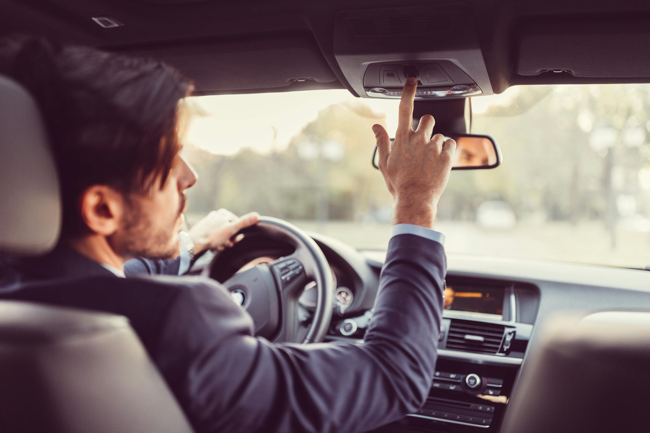 A picture from the back of a rideshare car as the driver messes with a button in the car, not paying attention while driving.