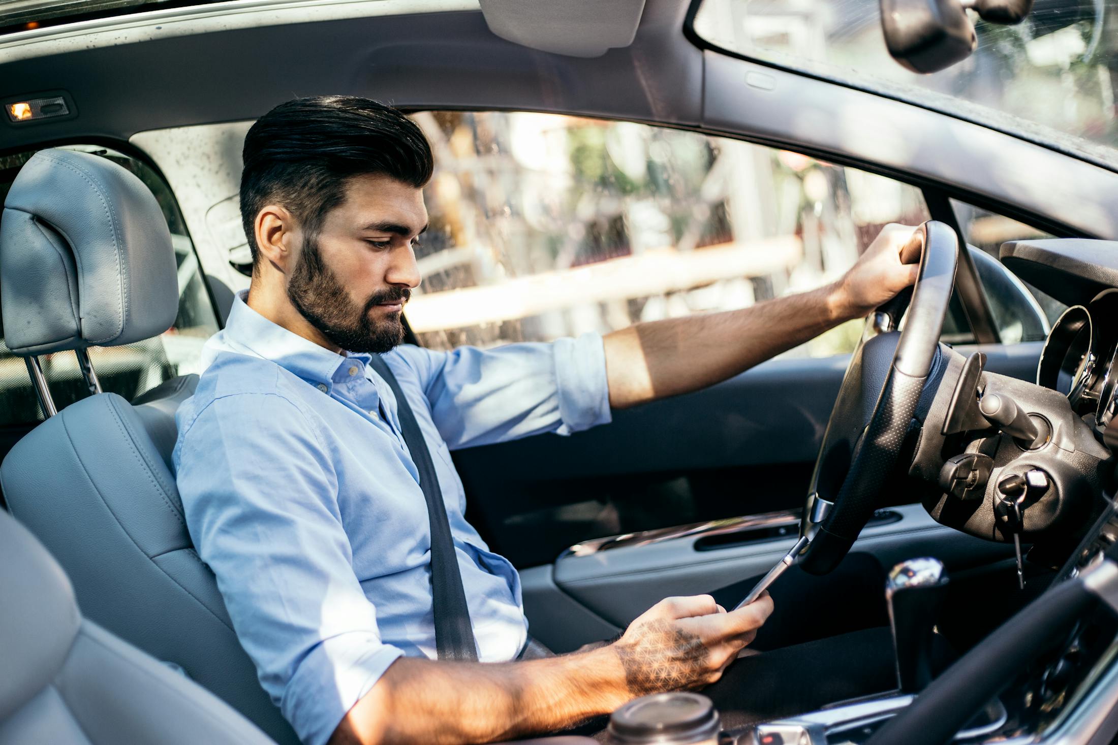 An uber driver is looking at his cell phone instead of the road while driving the car.