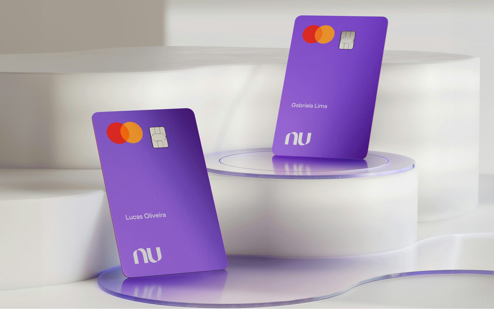 Dois cartões do Nubank vistos de frente postos sob superfícies geométricas circulares. Os cartões estão com a face principal virada para cima, com o logo da bandeira Mastercard, chip e nomes dos clientes.