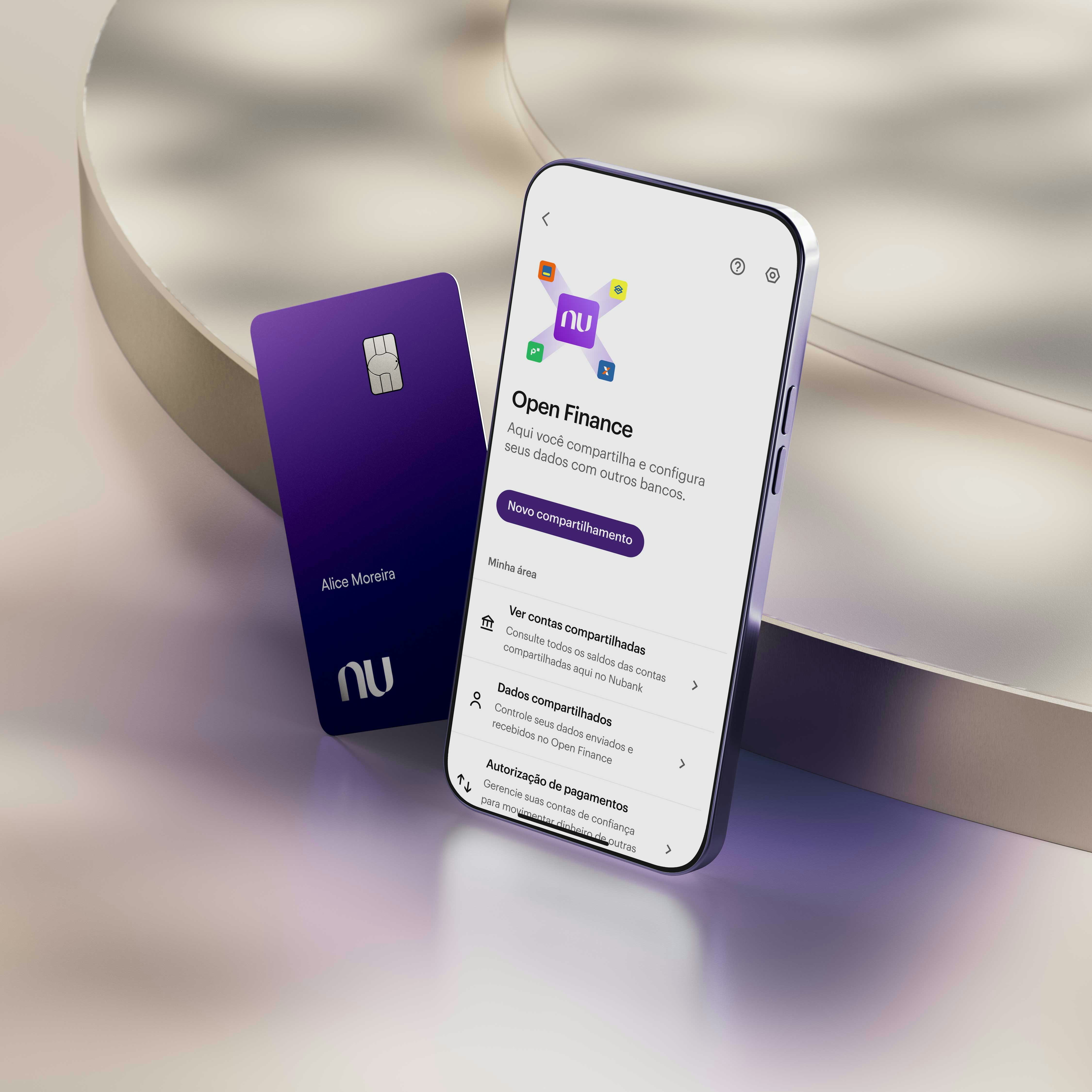 Apoiados em uma plataforma metalizada circular iluminada por uma luz roxa há um smartphone na seção Open Finance em sua tela e um Cartão Ultravioleta Black do Nubank com o nome Alice Moreira.