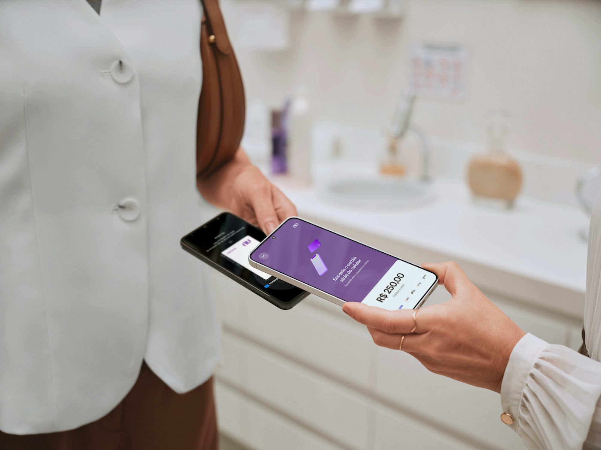 Imagem foca nas mãos de duas pessoas realizando uma transação de pagamento com os seus celulares. Em um dos celulares, é possível ver a tela do Tap to Pay do Nu Empresas.