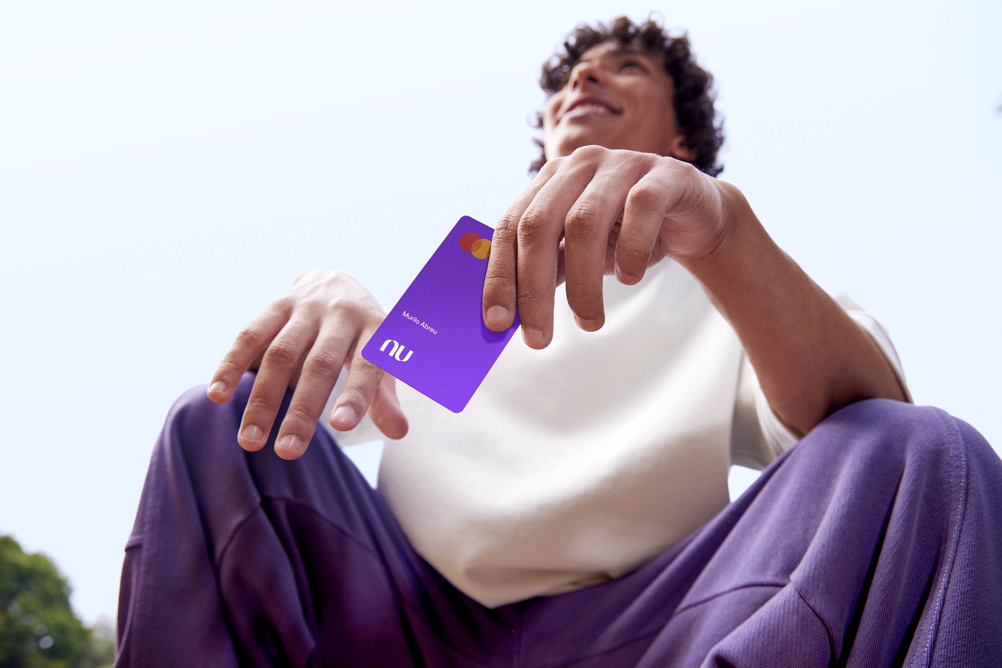 Na imagem aparece um menino segurando o cartão do Nubank Roxinho.
