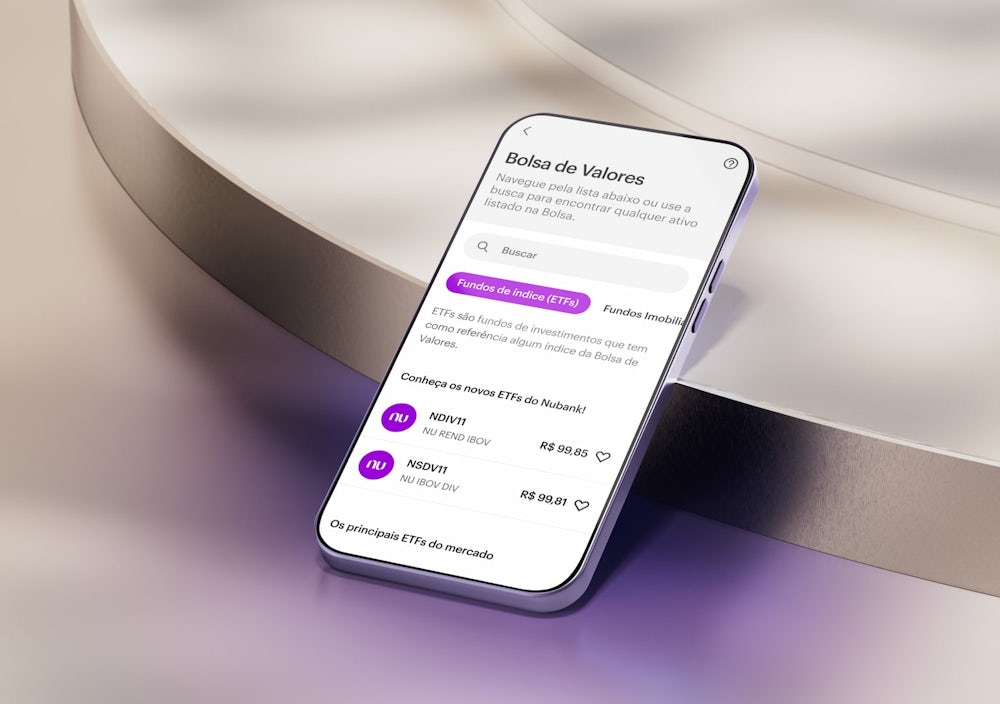 A tela de um celular apoiado em uma forma geométrica em tons claros. Na tela, o aplicativo do Nubank na área de Bolsa de Valores.