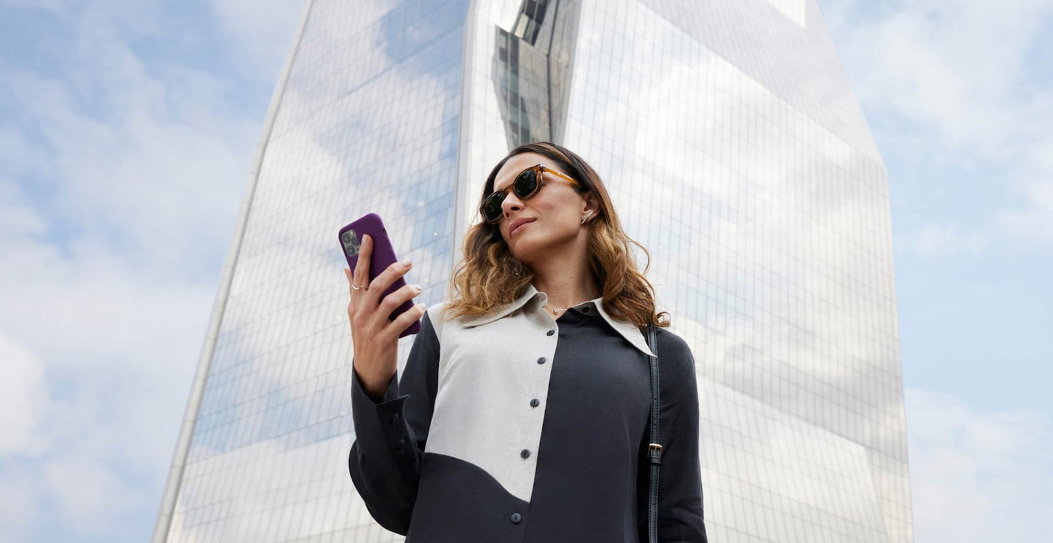 Mulher olhando para o celular em frente a prédio arquitetônico