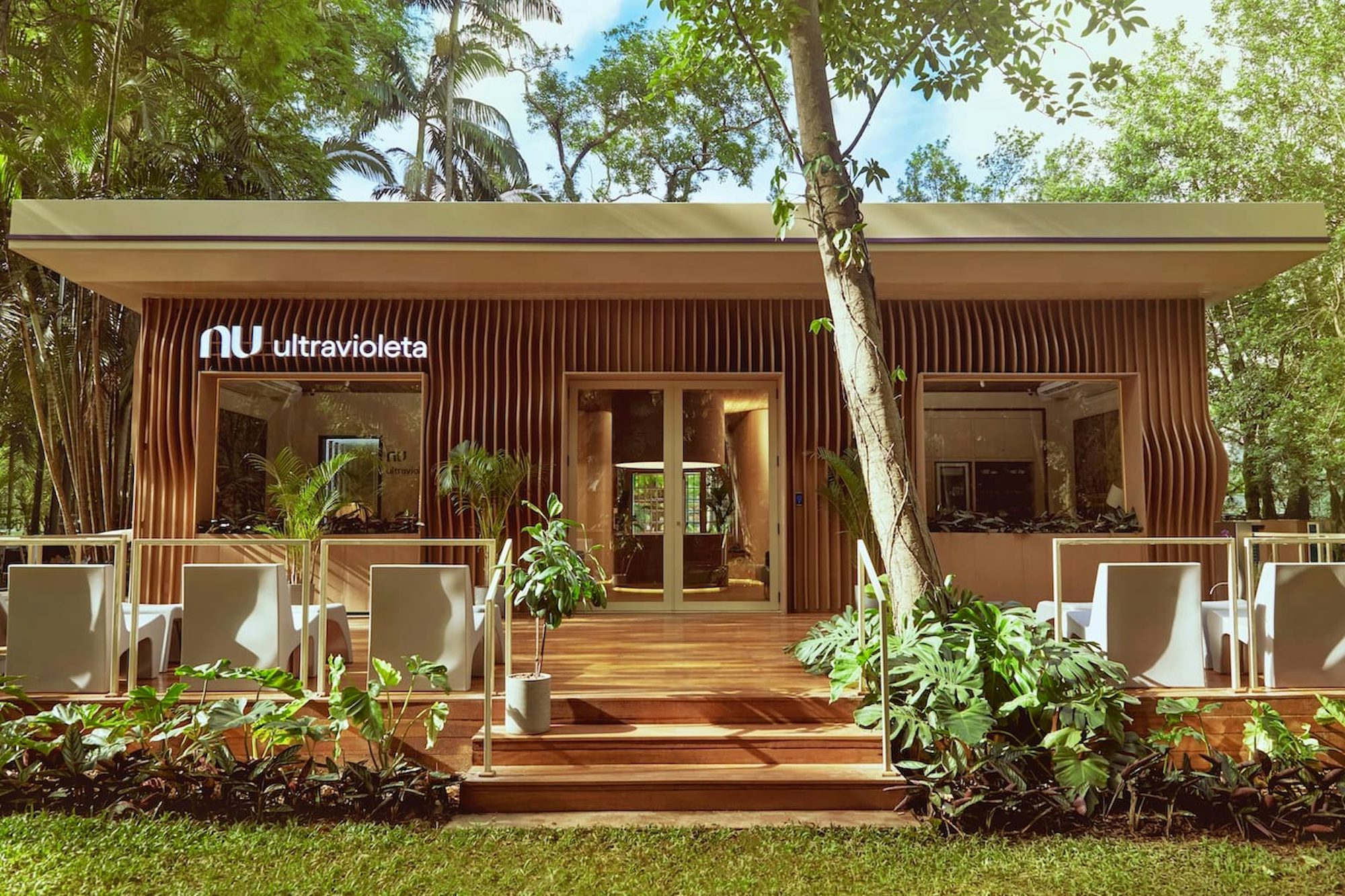 Foto da fachada da Casa Nubank Ultravioleta, no Ibirapuera. Toda de madeira, com o logo do Nu e o nome Ultravioleta na frente. Com uma pequena área verde na frente.
