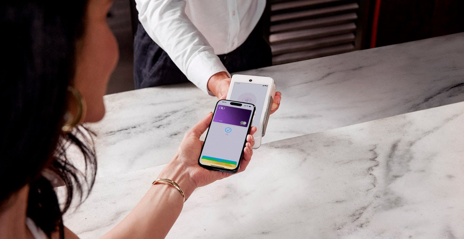 Mulher efetuando o pagamento por aproximação através do cartão Ultravioleta no Samgung Pay em uma doceria, enquanto o atendente segura a maquininha do cartão.