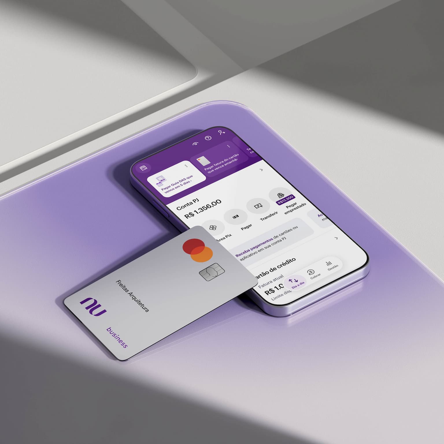 Celular com aplicativo Nubank aberto na tela ao lado de um cartão de crédito PJ. O celular e o cartão estão apoiados em uma forma geométrica.