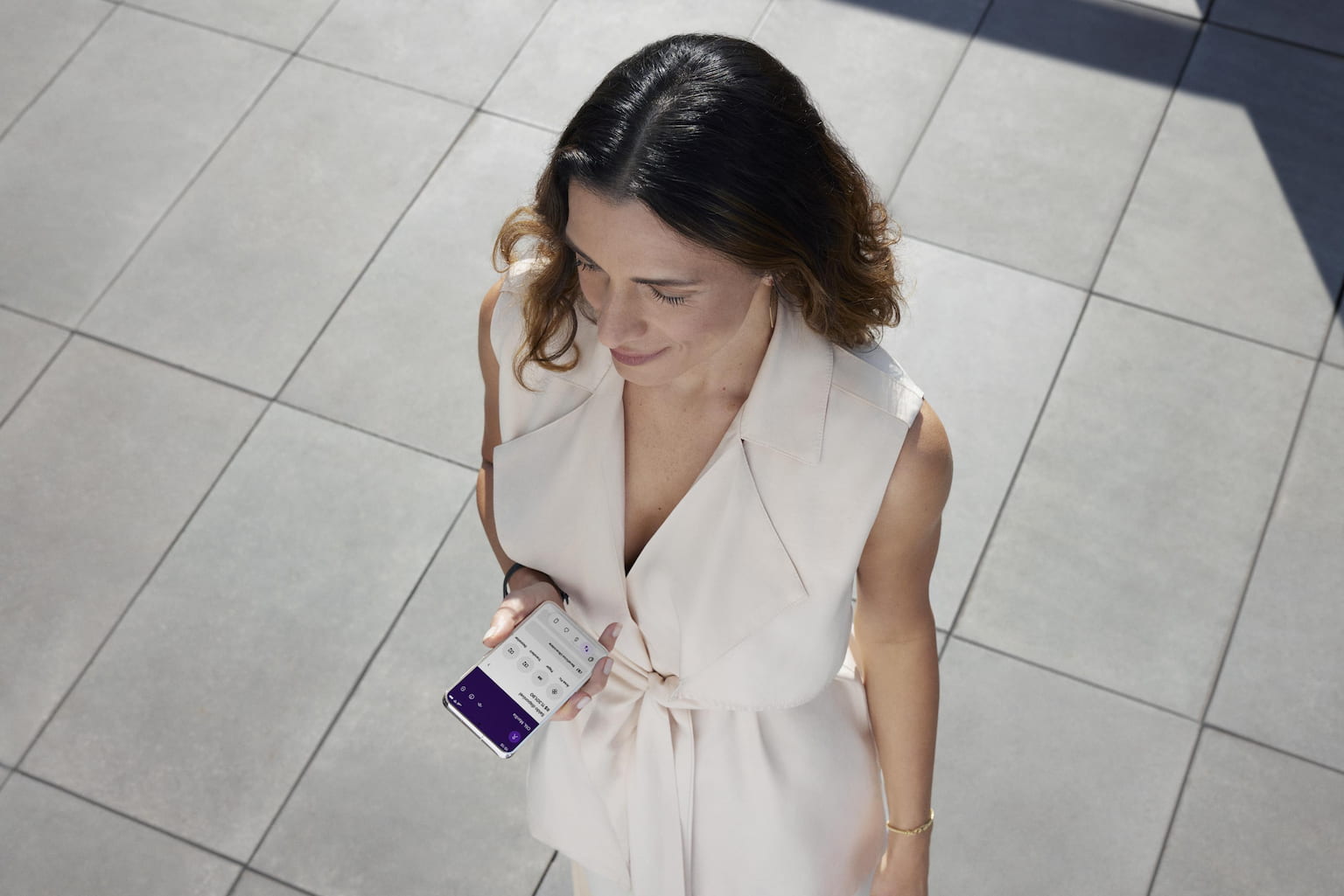 Vista de cima mostra uma mulher branca segurando o celular com a mão esquerda e olhando para frente. Na tela do celular, a sua conta Nu.