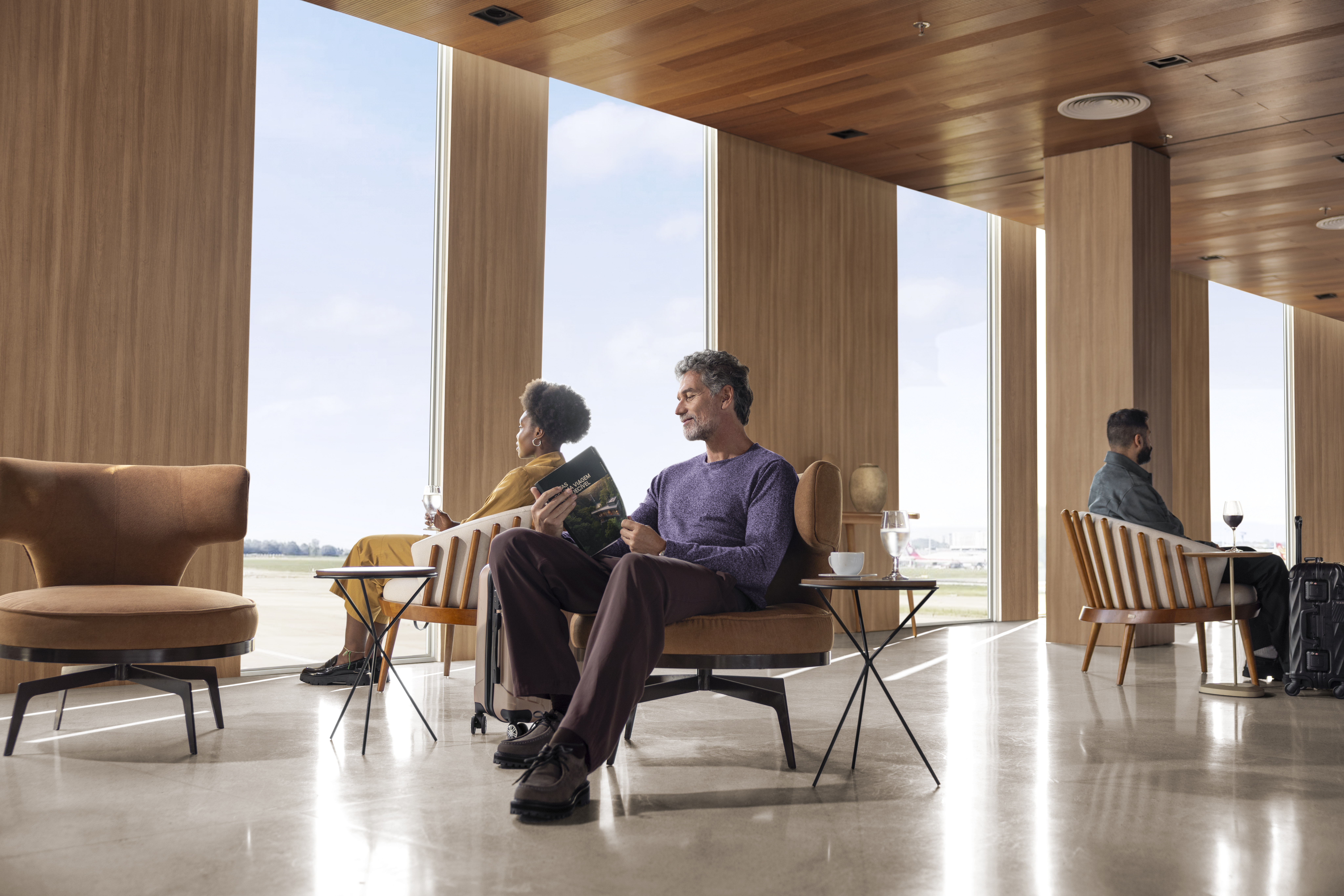 Homem branco com um folheto de viagens na mão sentado na Sala VIP