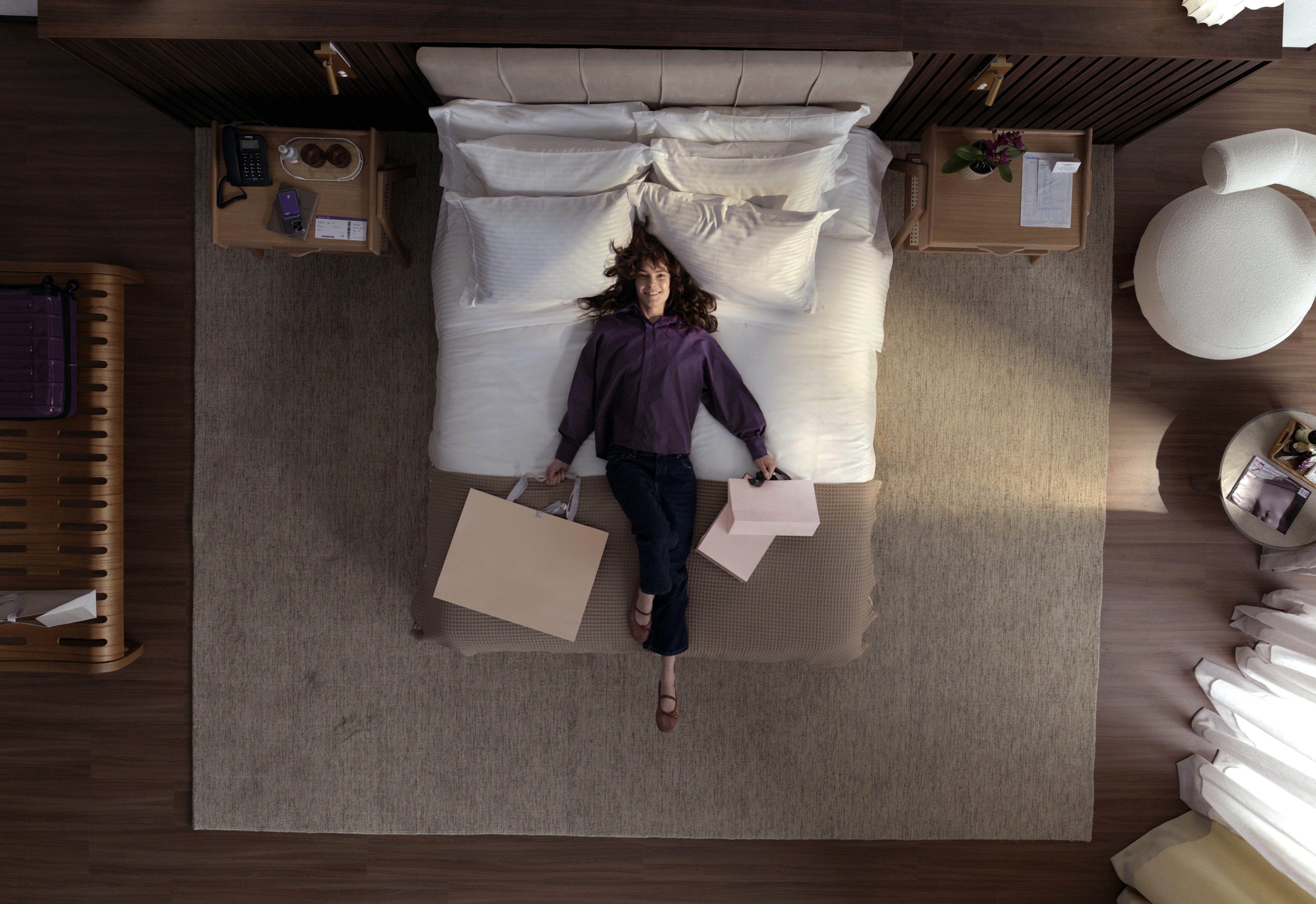Mulher deitada na cama do hotel com bolsas de compras