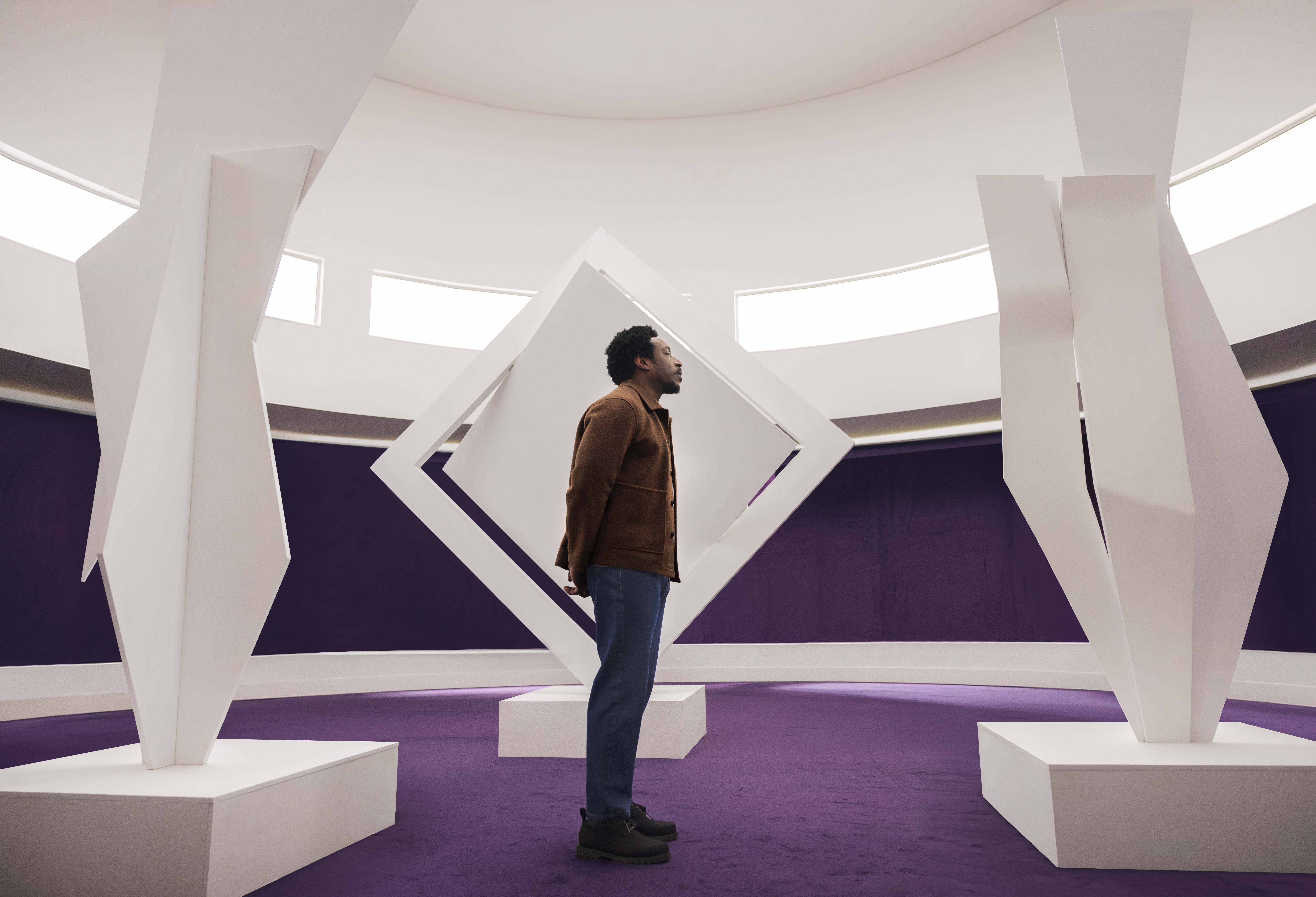 Homem negro em um cenário roxo observando esculturas de arte