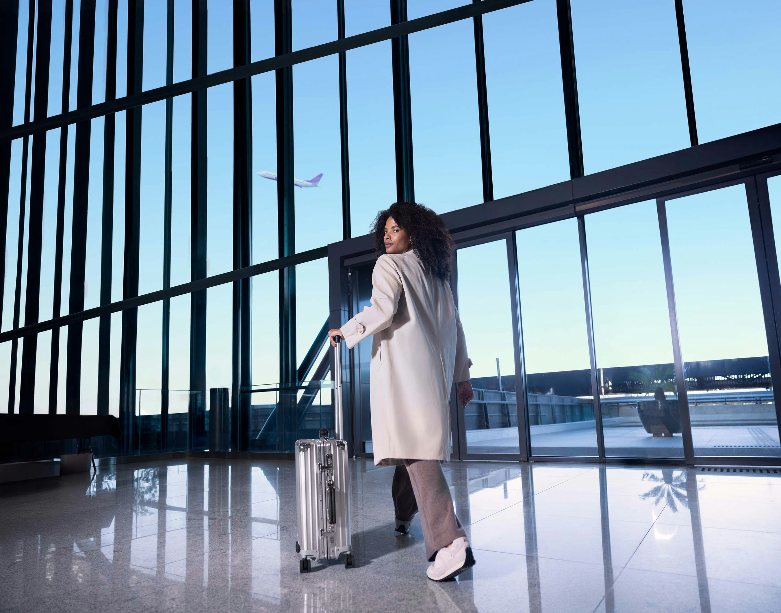 Mulher negra caminhando no aeroporto com sua mala de viagem.