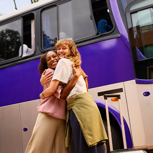 Duas amigas se abraçando na frente de um ônibus