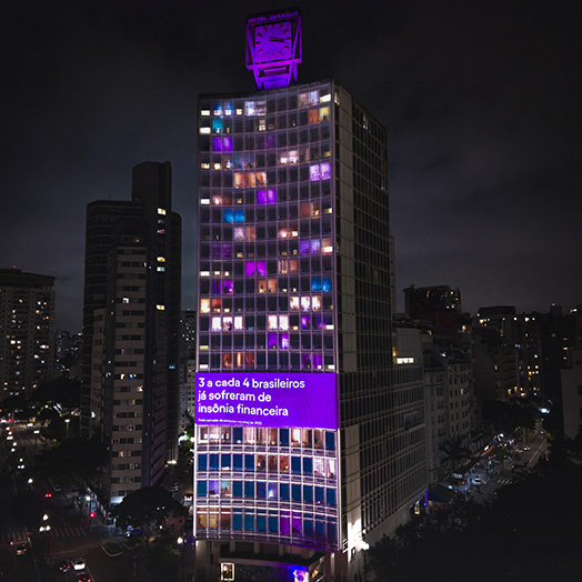 Uma projeção à noite no centro de São Paulo escrito "3 a cada 4 pessoas já sofreram de insônia financeira"