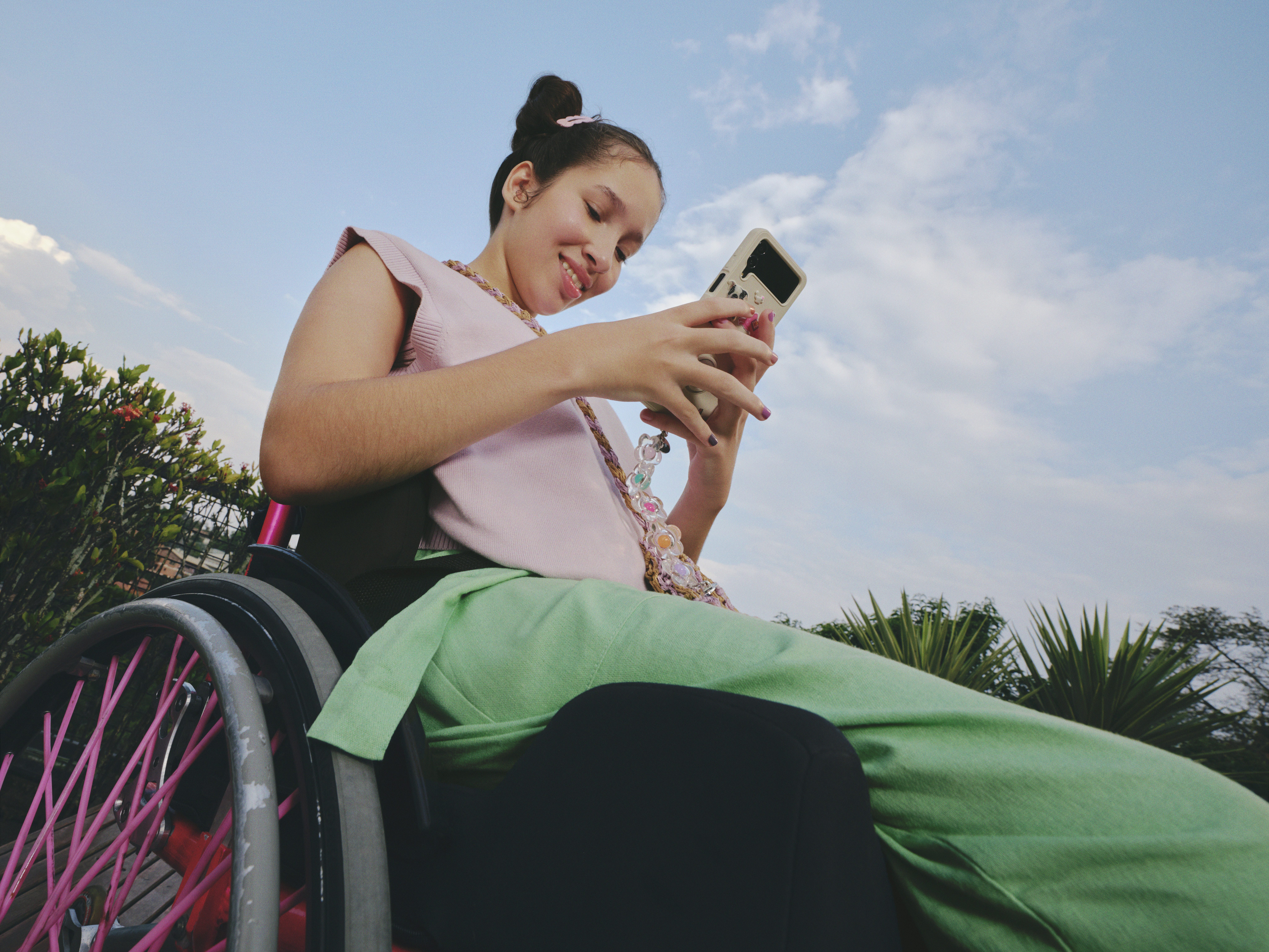Uma menina caderante usando blusa rosa e calça verde mexendo no celular
