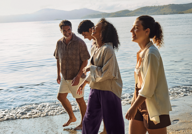 Um grupo de quatro pessoas caminhando na areia da praia, próximos ao mar.