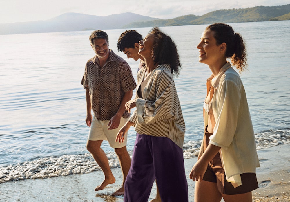 Um grupo de quatro pessoas caminhando na areia da praia, próximos ao mar.
