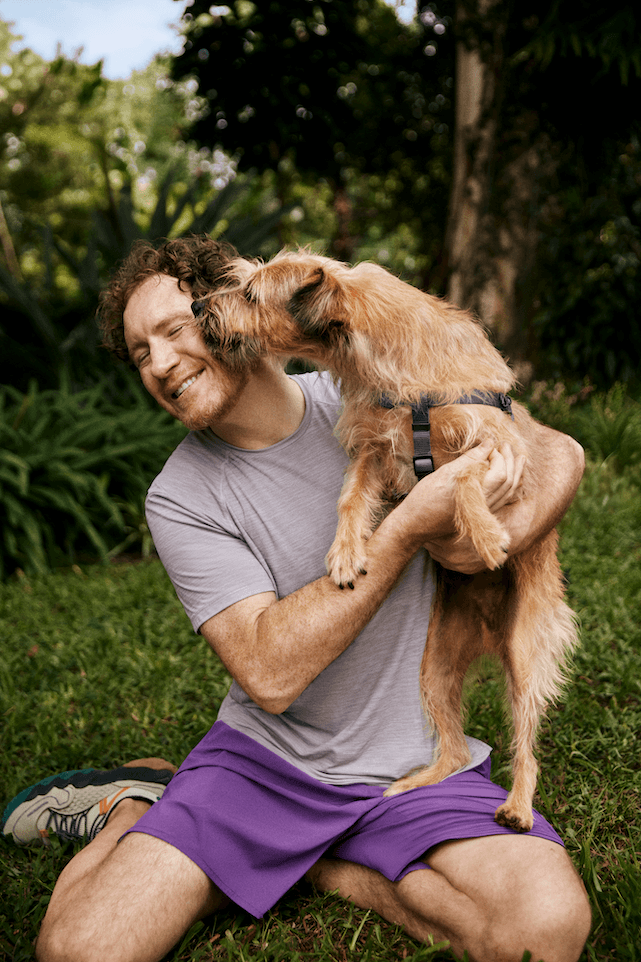 Homem com o cachorro no colo que está lambendo seu rosto