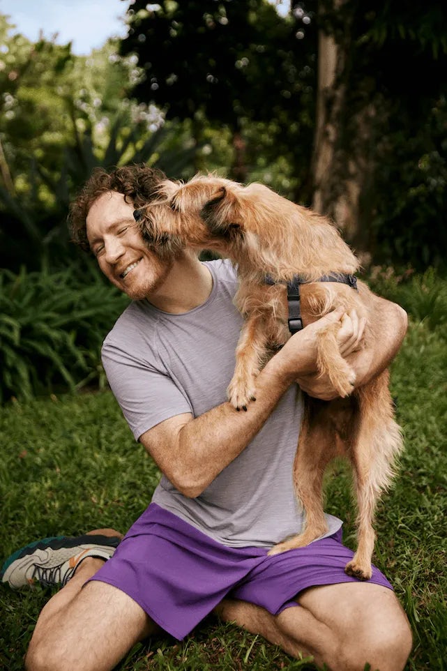 Homem com o cachorro no colo que está lambendo seu rosto