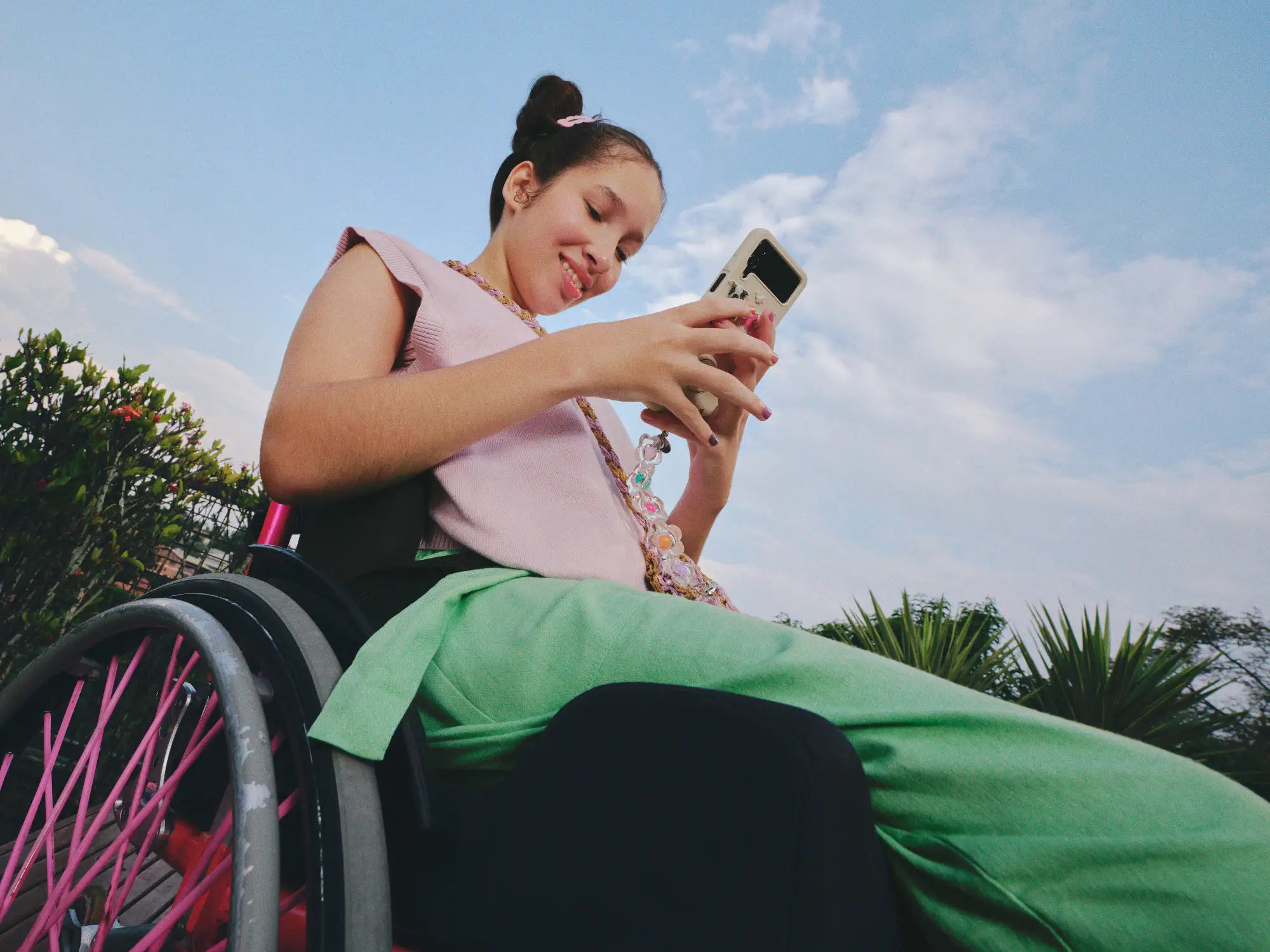 Uma menina caderante usando blusa rosa e calça verde mexendo no celular