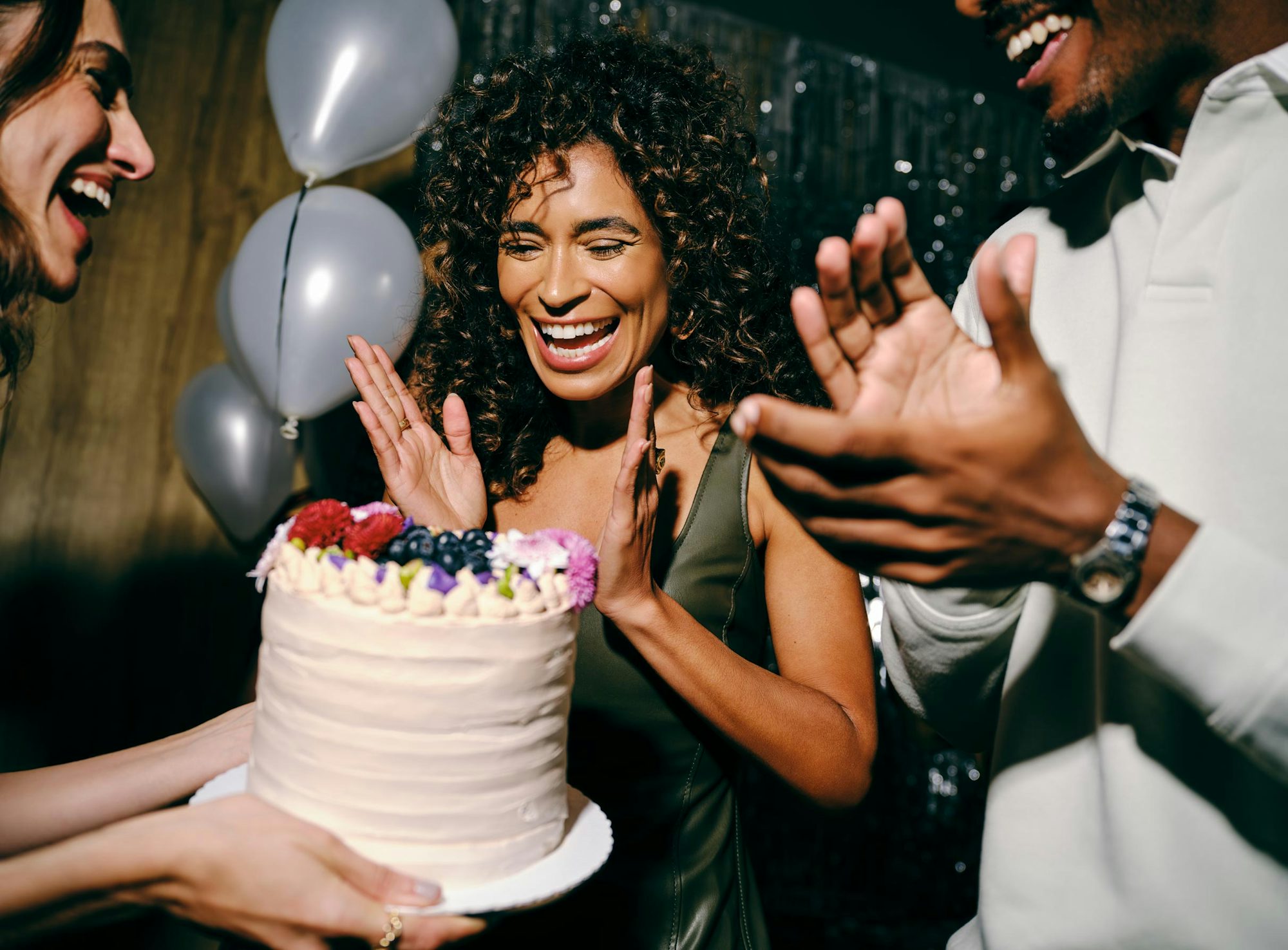 Mulher sorrindo ao receber um bolo de aniversário em festa.
