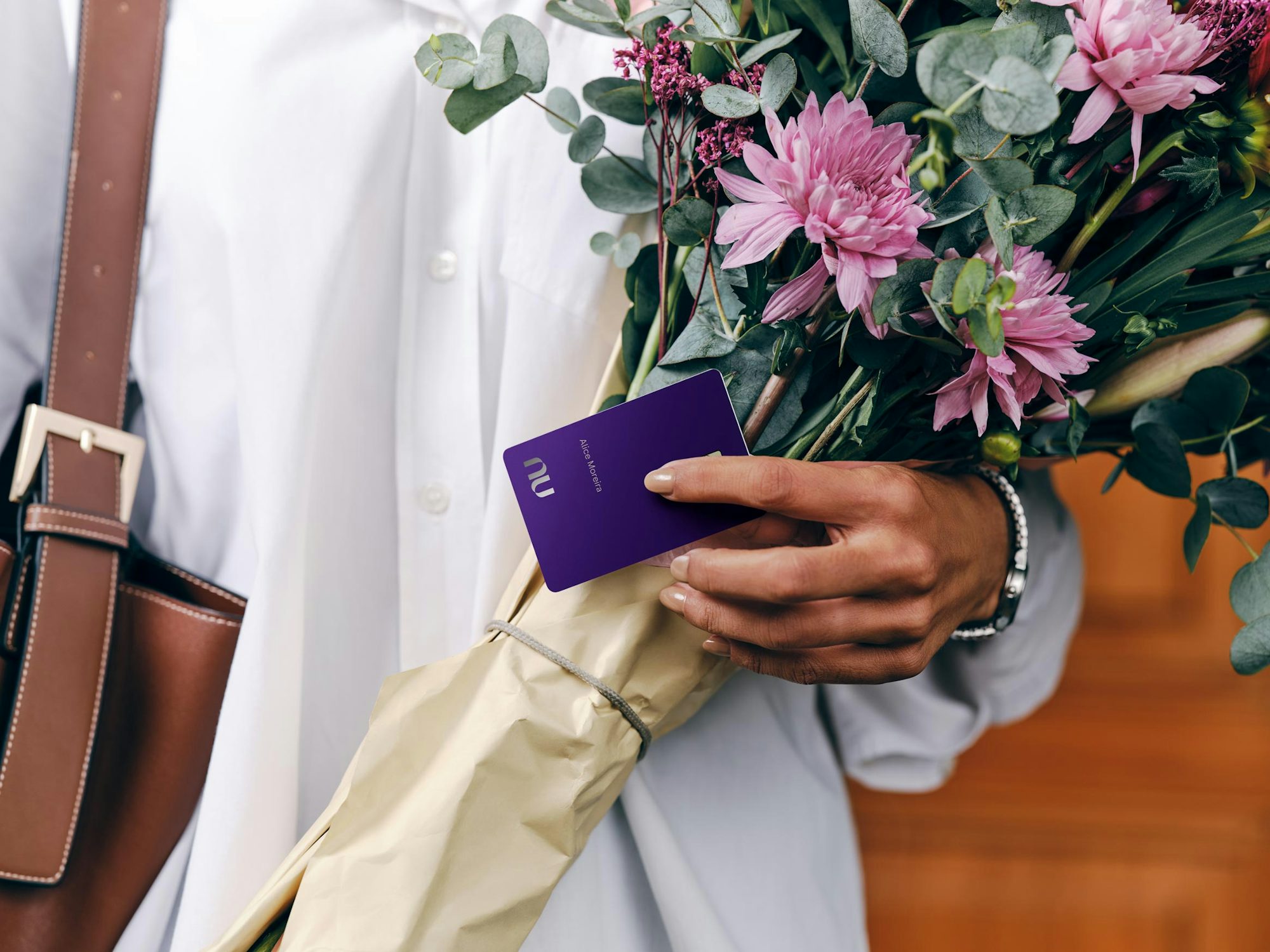 Pessoa segurando cartão Nubank Ultravioleta e um buquê de flores.