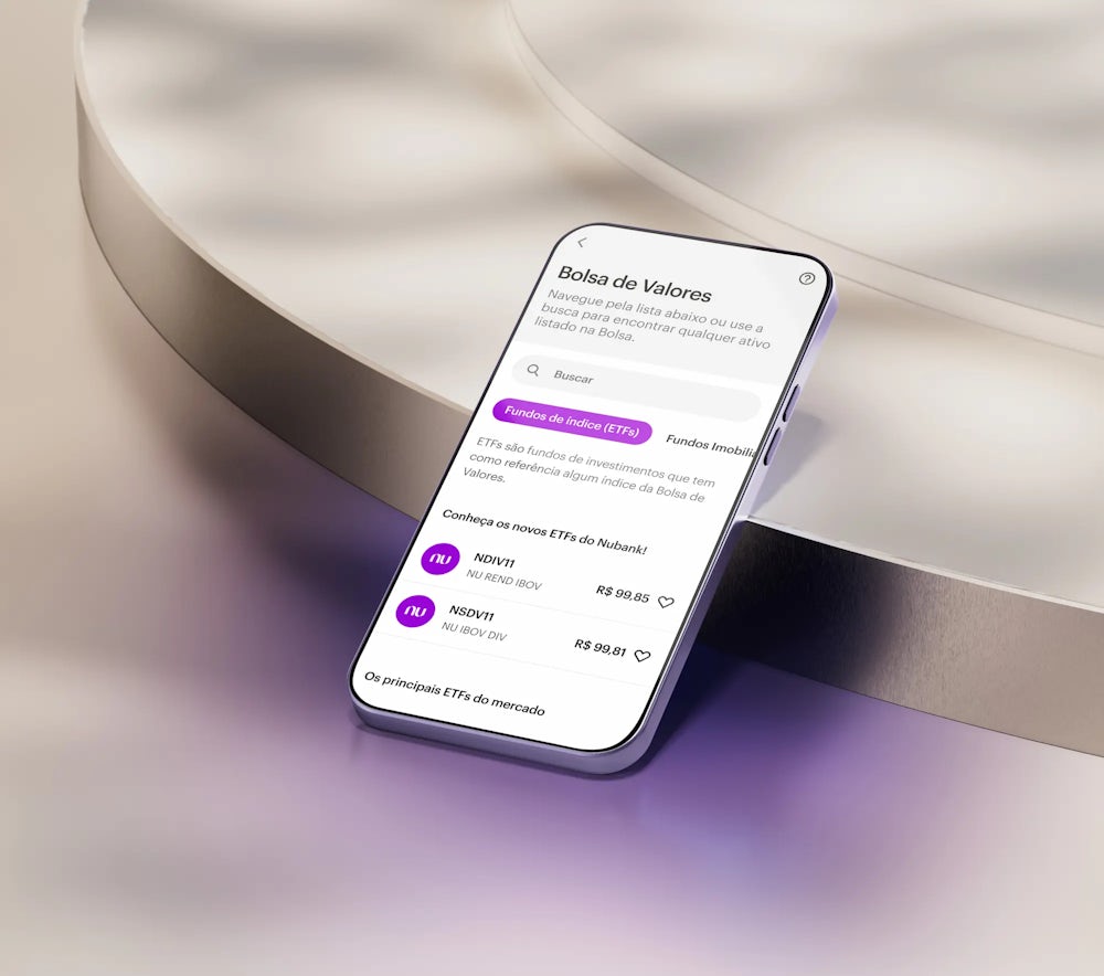 A tela de um celular apoiado em uma forma geométrica em tons claros. Na tela, o aplicativo do Nubank na área de Bolsa de Valores.