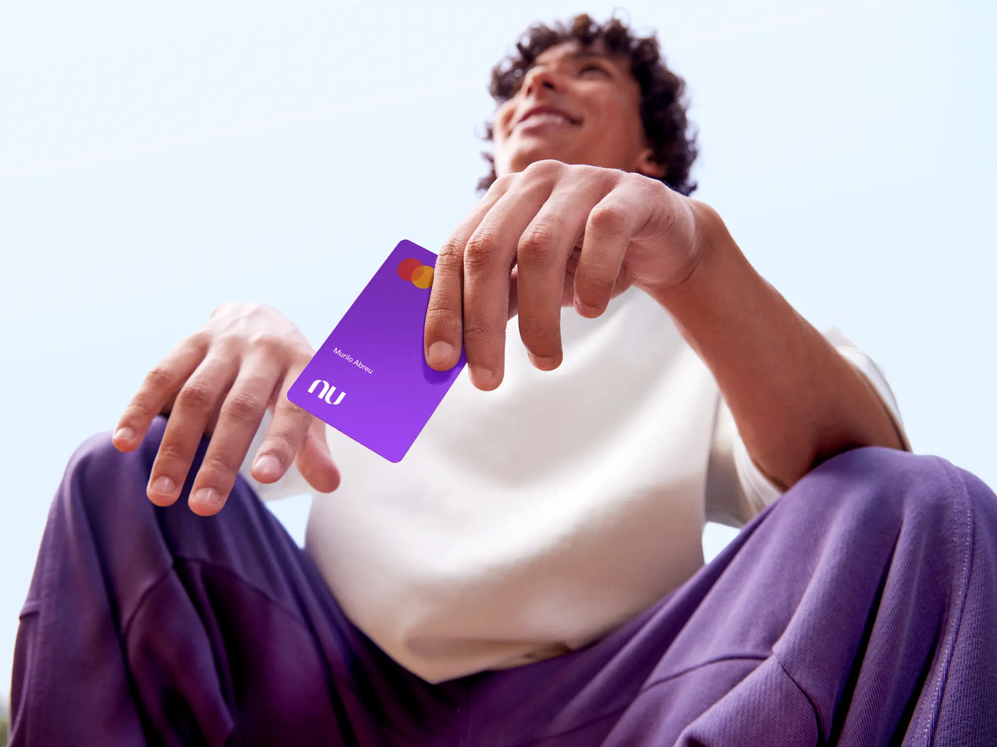 Na imagem aparece um menino segurando o cartão do Nubank Roxinho.