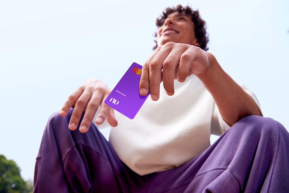 Na imagem aparece um menino segurando o cartão do Nubank Roxinho.