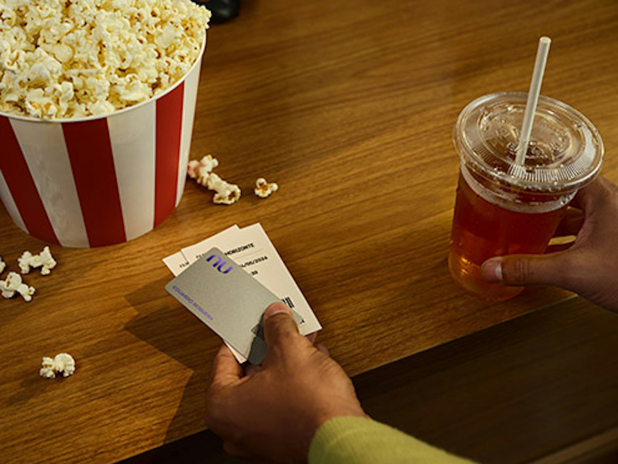 Na foto podemos ver a mão de um homem realizando o pagamento de uma pipoca e refrigerantes no cinema com o cartão virtual Nubank Croma em seu celular