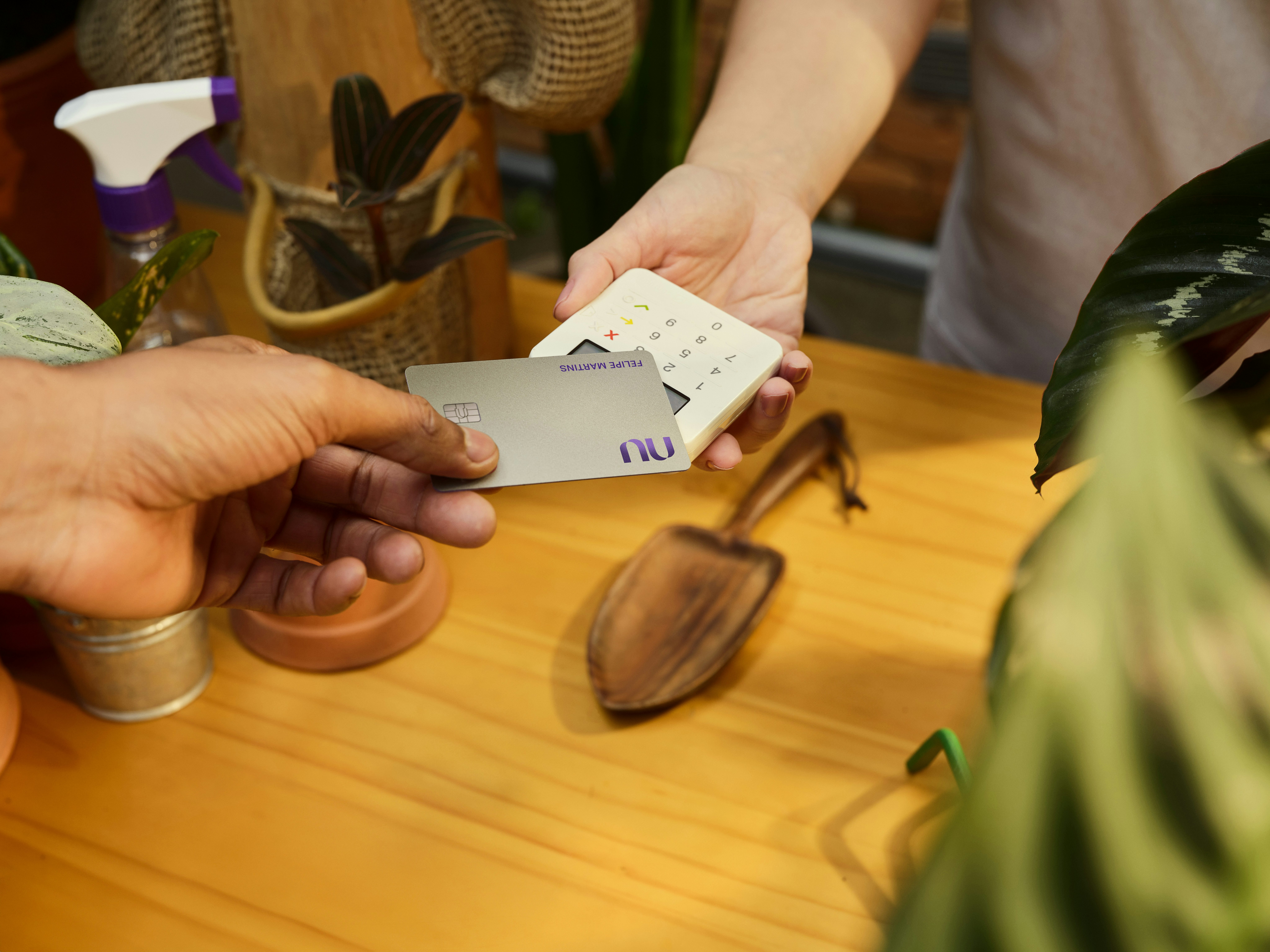 Pessoa aproxima um cartão Nubank Croma de uma maquininha para realizar um pagamento por aproximação.